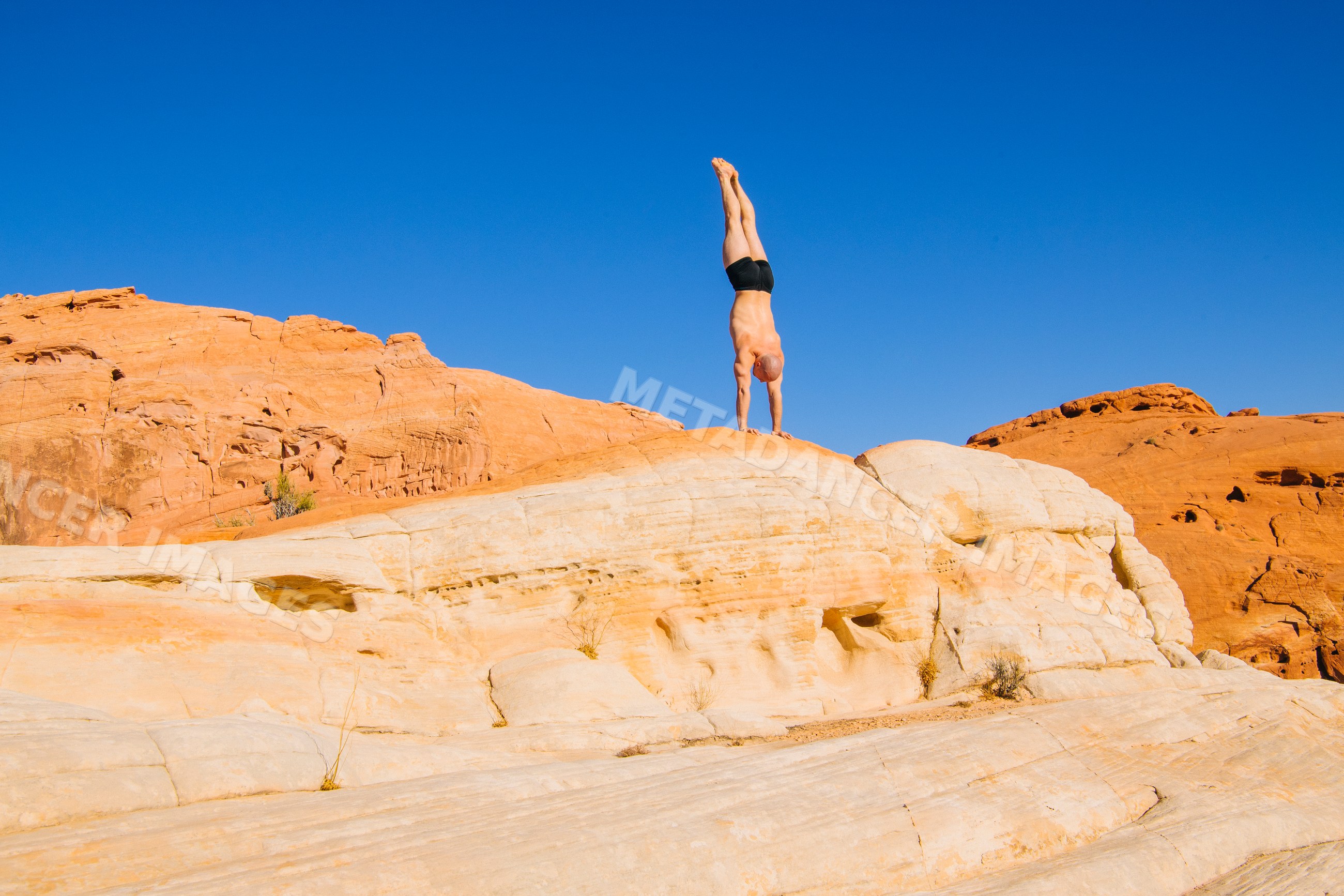 White person doing handstand on desert rock formation