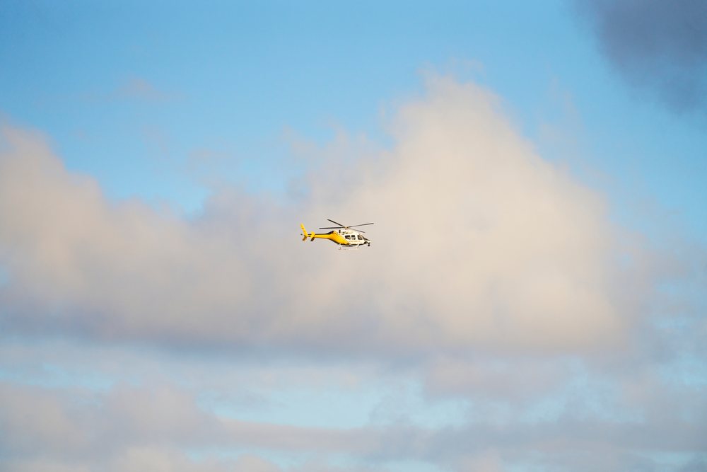 Yellow helicopter flying in partly cloudy sky