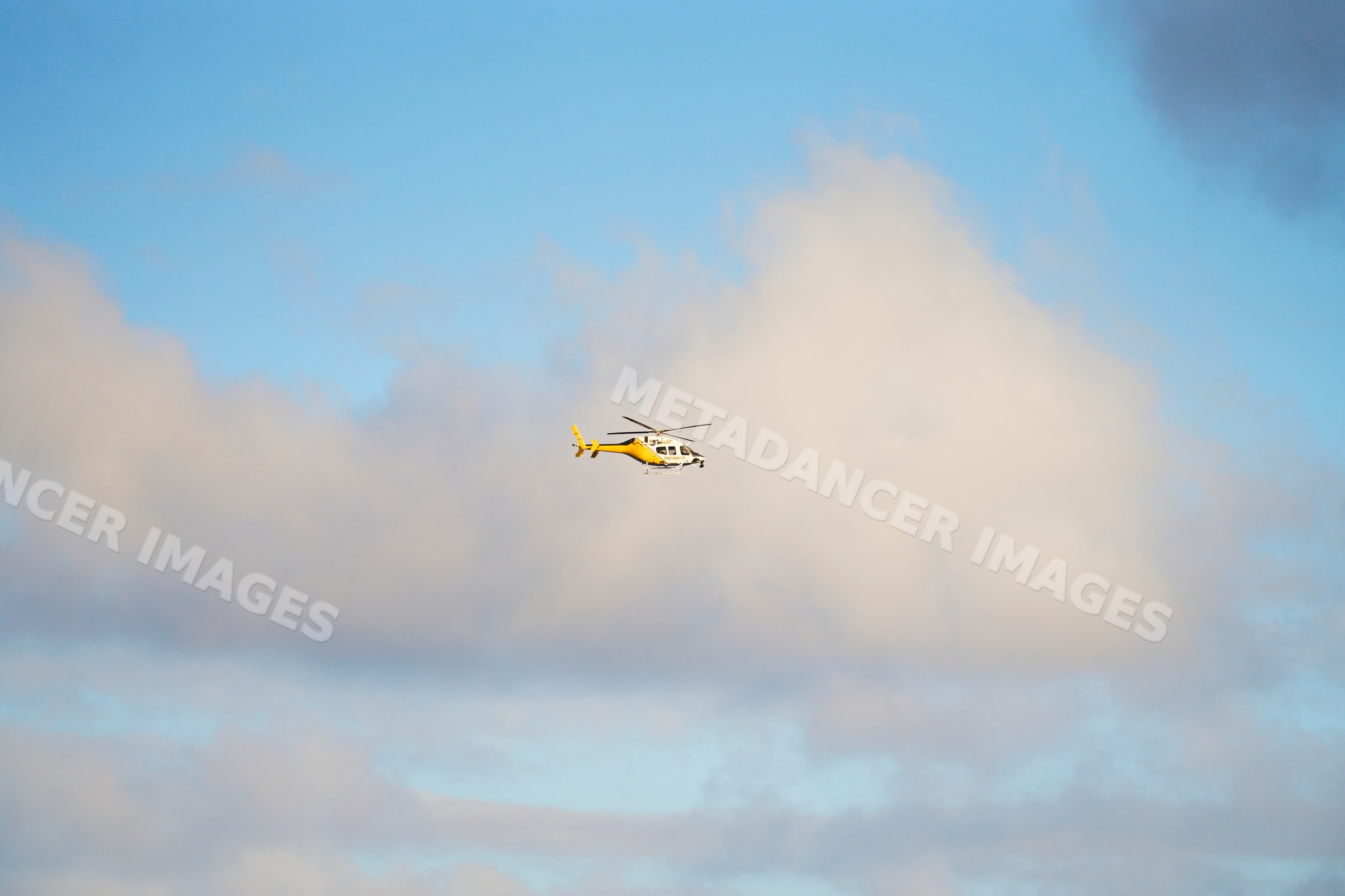 Yellow helicopter flying in partly cloudy sky