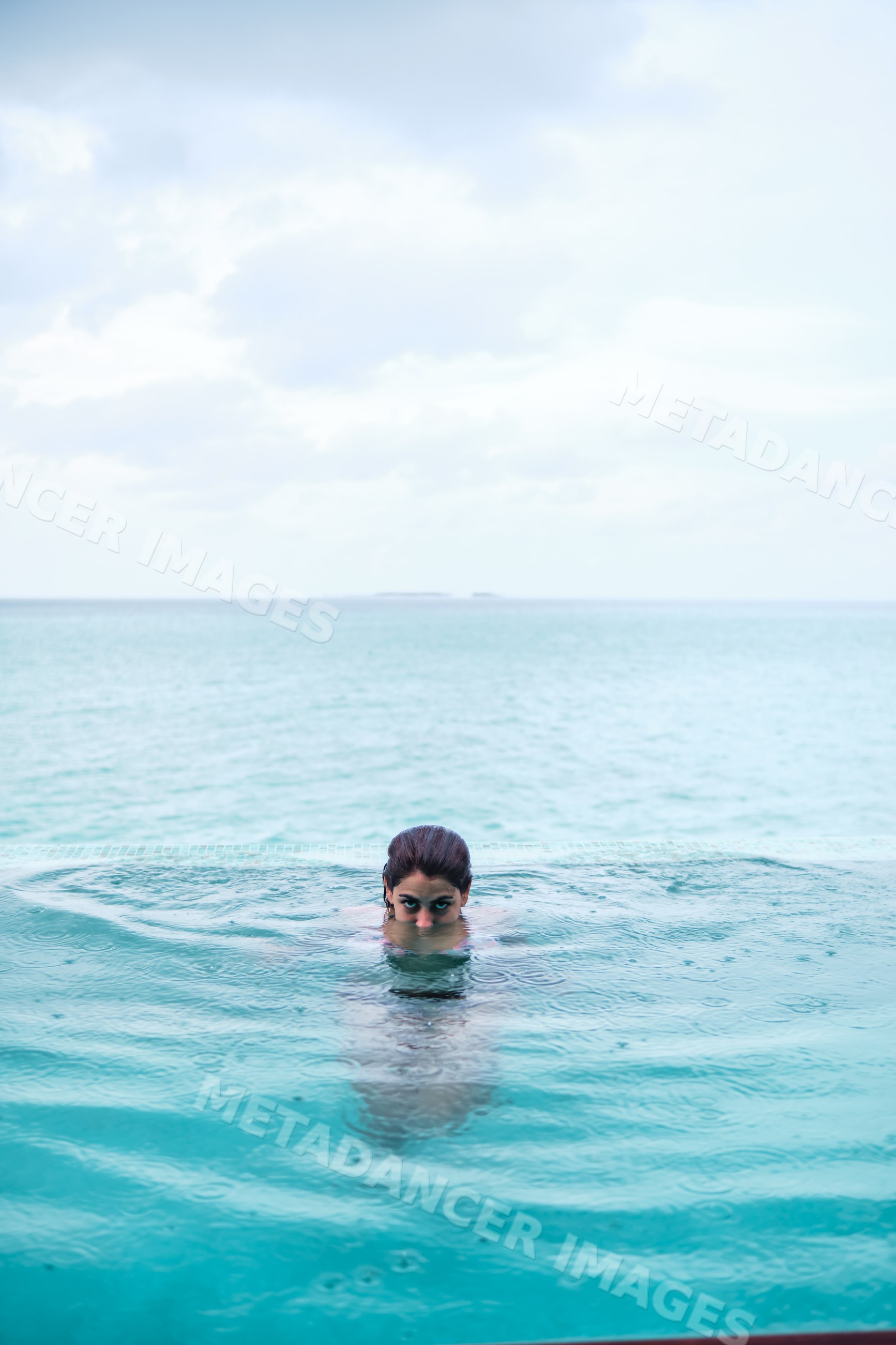 A white woman swimming in an infinity pool in the Maldives with ocean