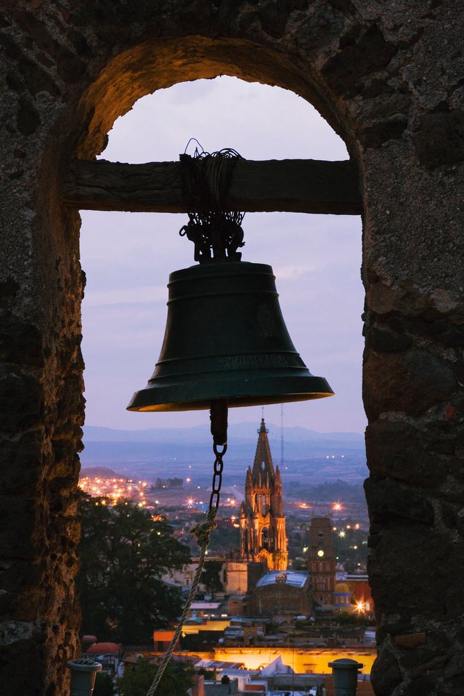 Bell in belfry arch overlooking church at twilight