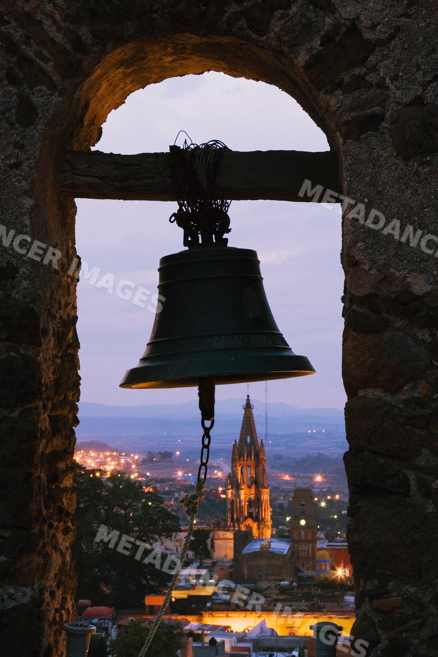 Bell in belfry arch overlooking church at twilight