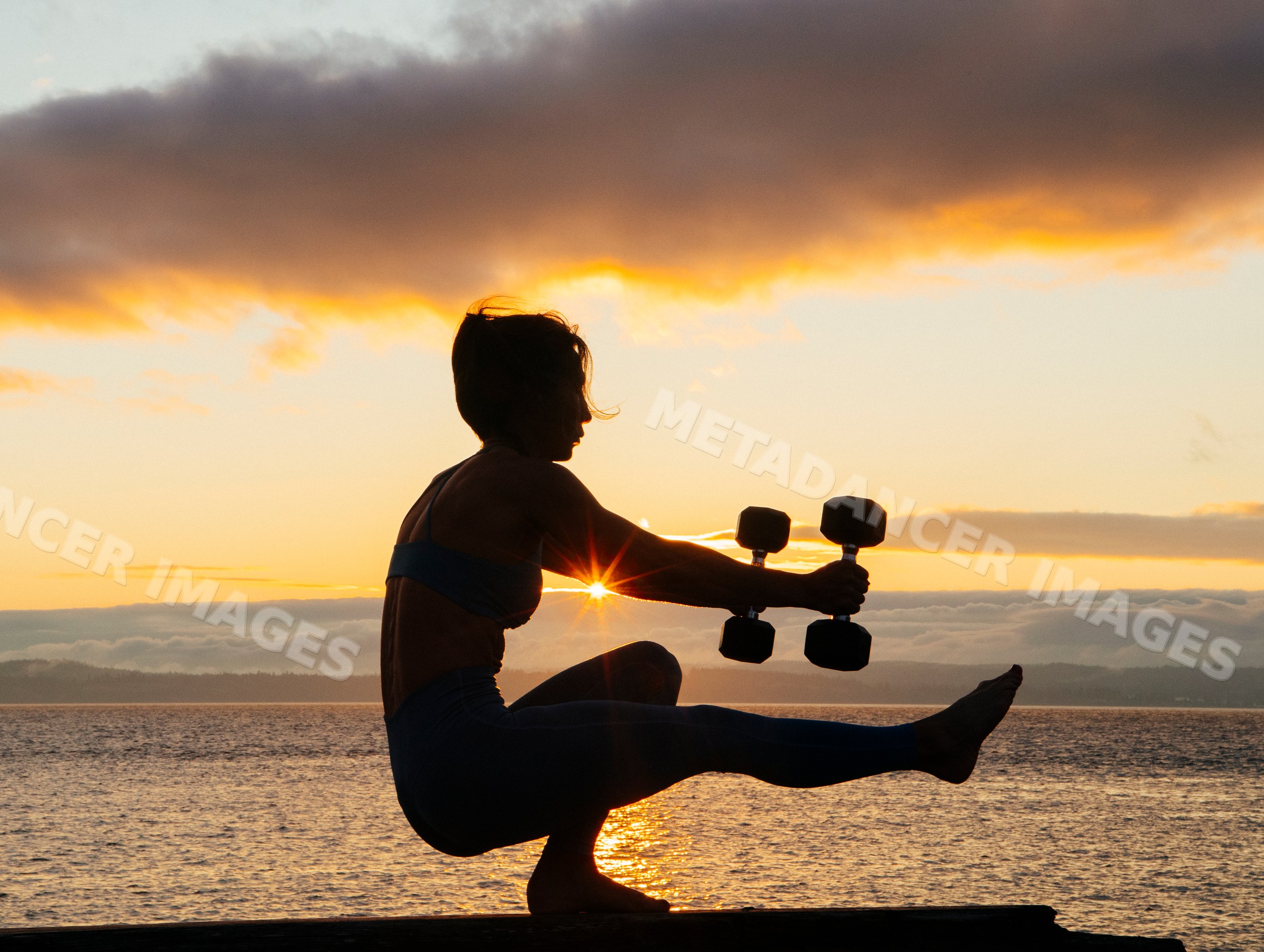 White woman exercising balancing with dumbbells at sunset by water