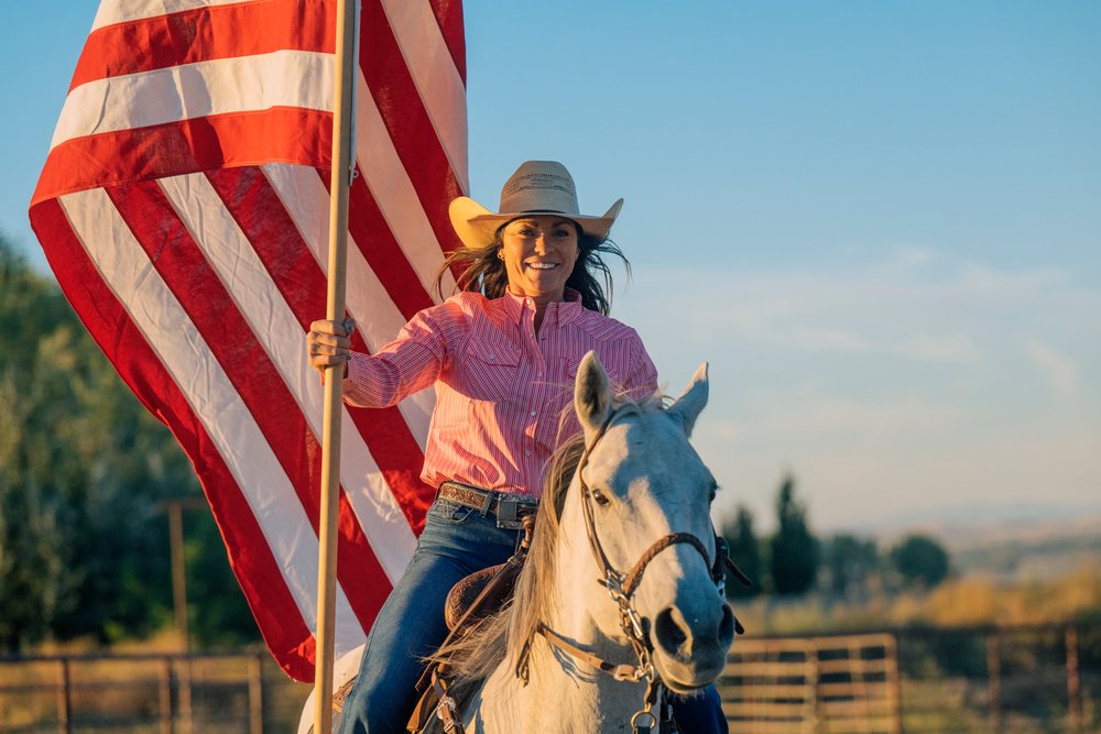 White woman horseback riding holding american flag