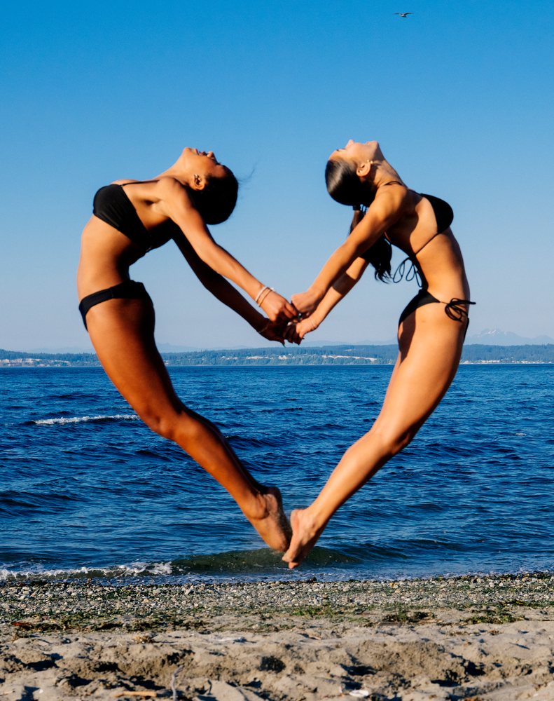Two women perform a synchronized jump holding hands on a beach