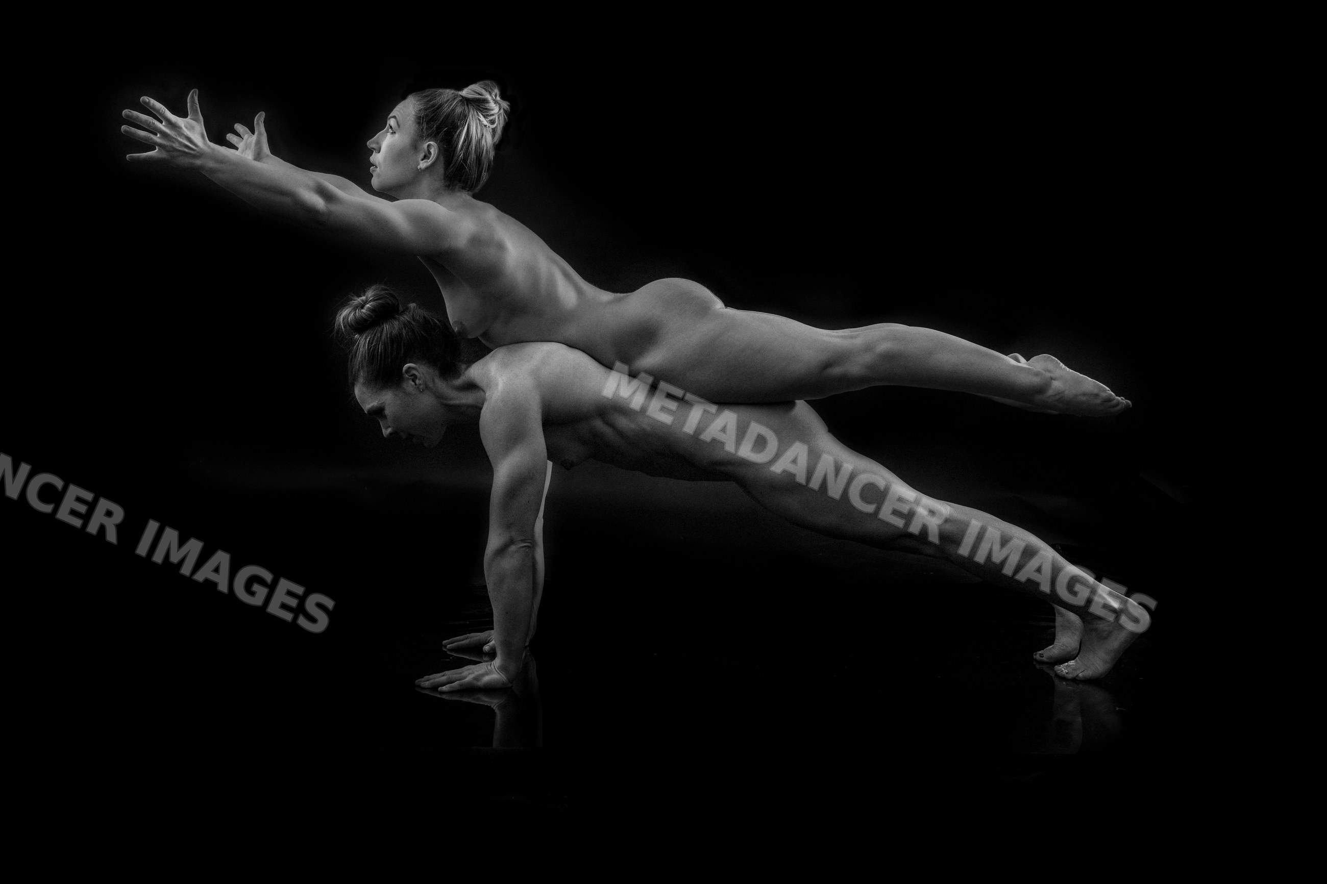 Two white women performing partner acrobatics yoga plank pose