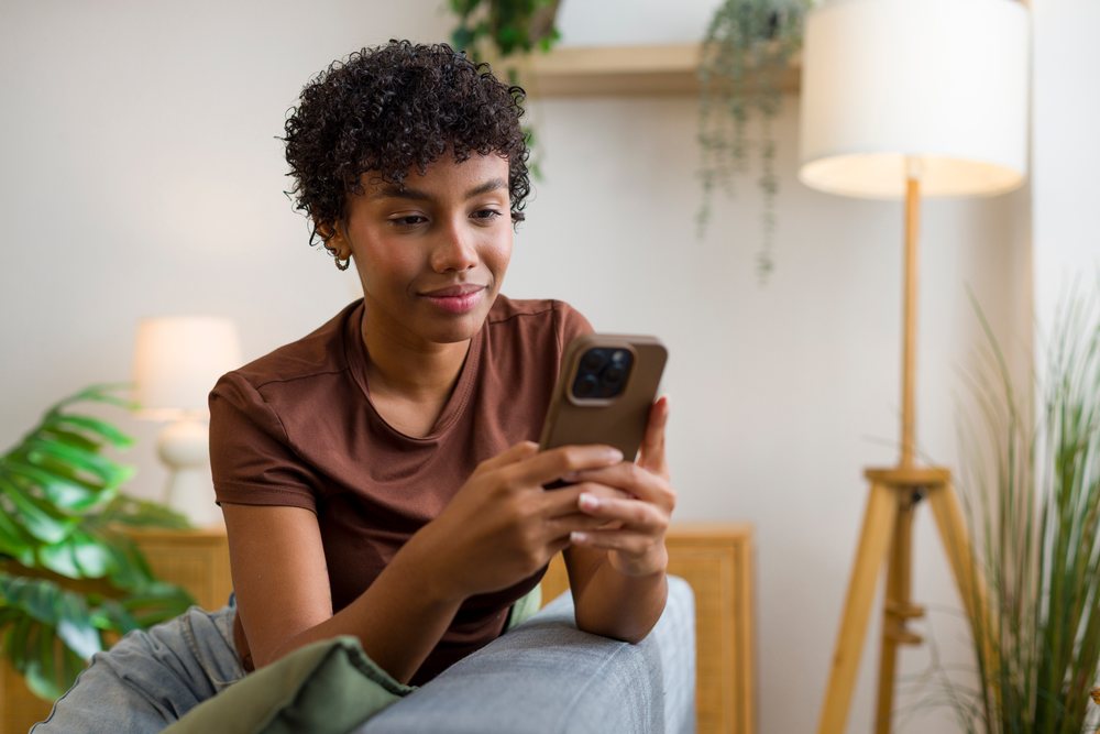 Young African American woman using smartphone at home on a couch