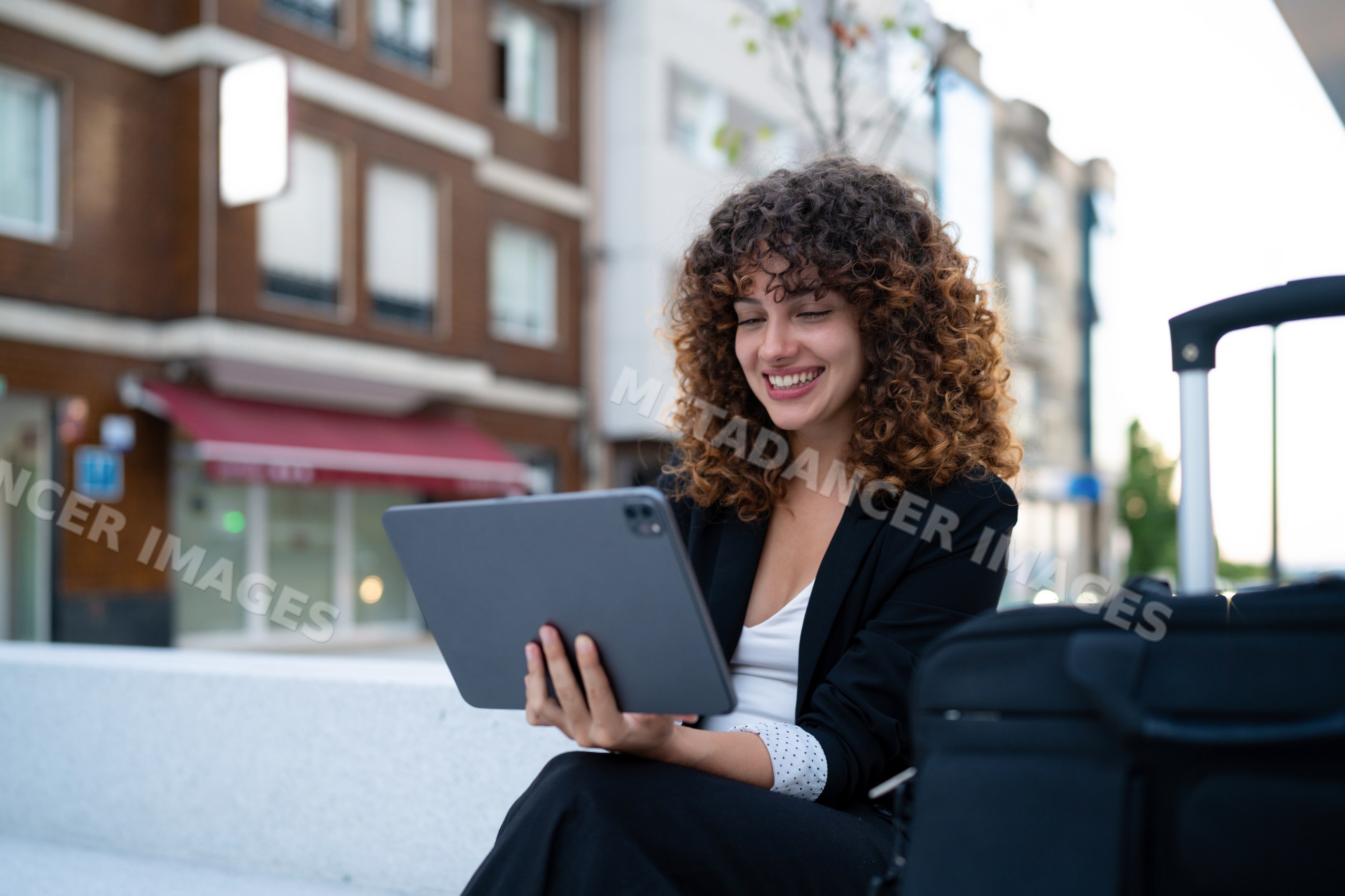 Young white woman using digital tablet outdoors with luggage