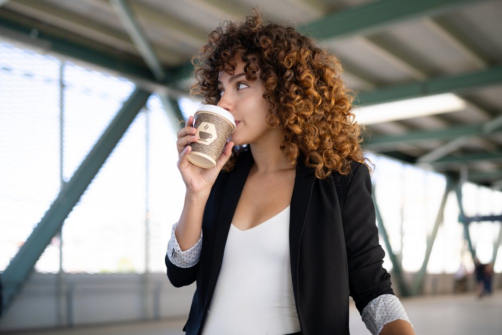 White woman drinking coffee from paper cup in urban outdoor space