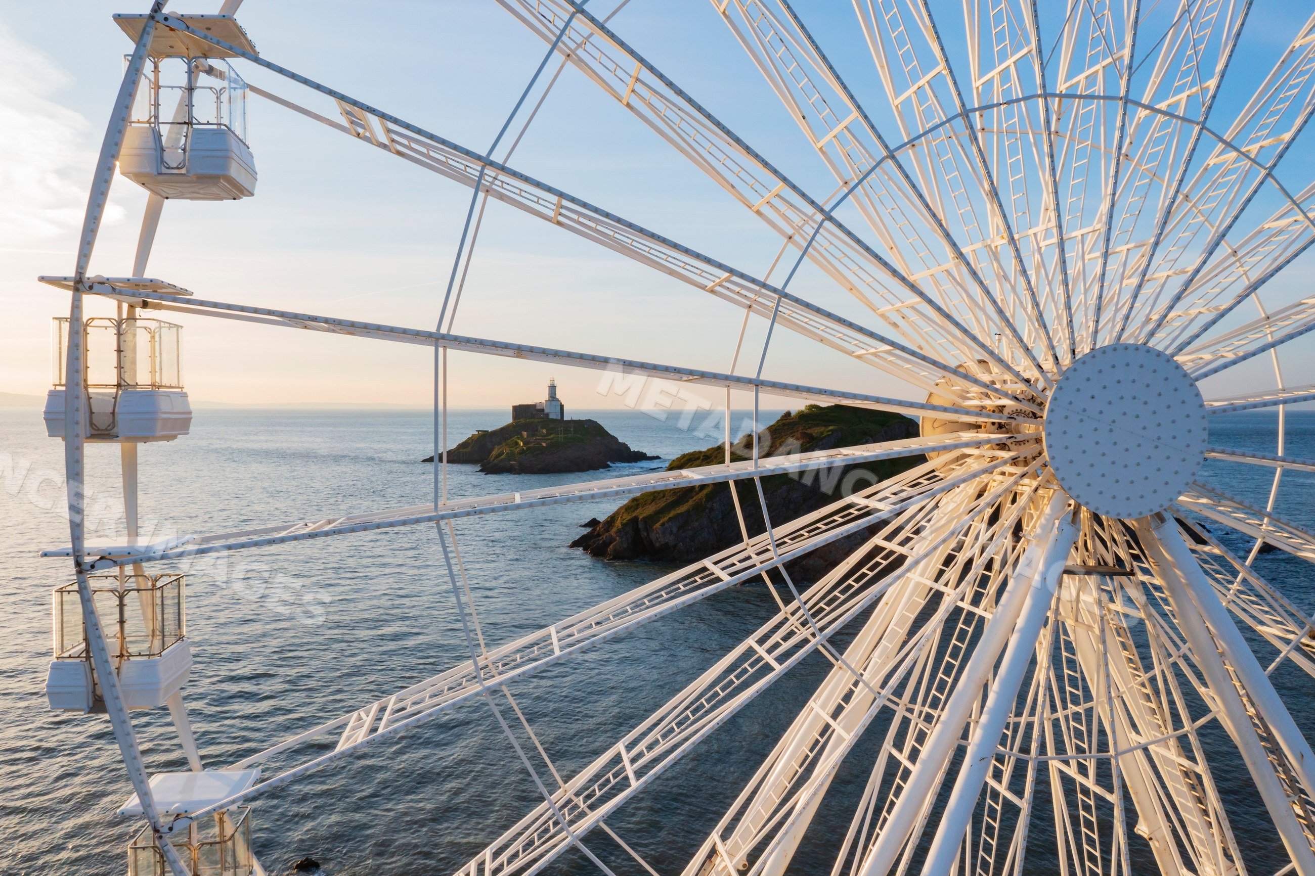 Ferris Wheel cabins and Mumbles Lighthouse at sunset in Wales