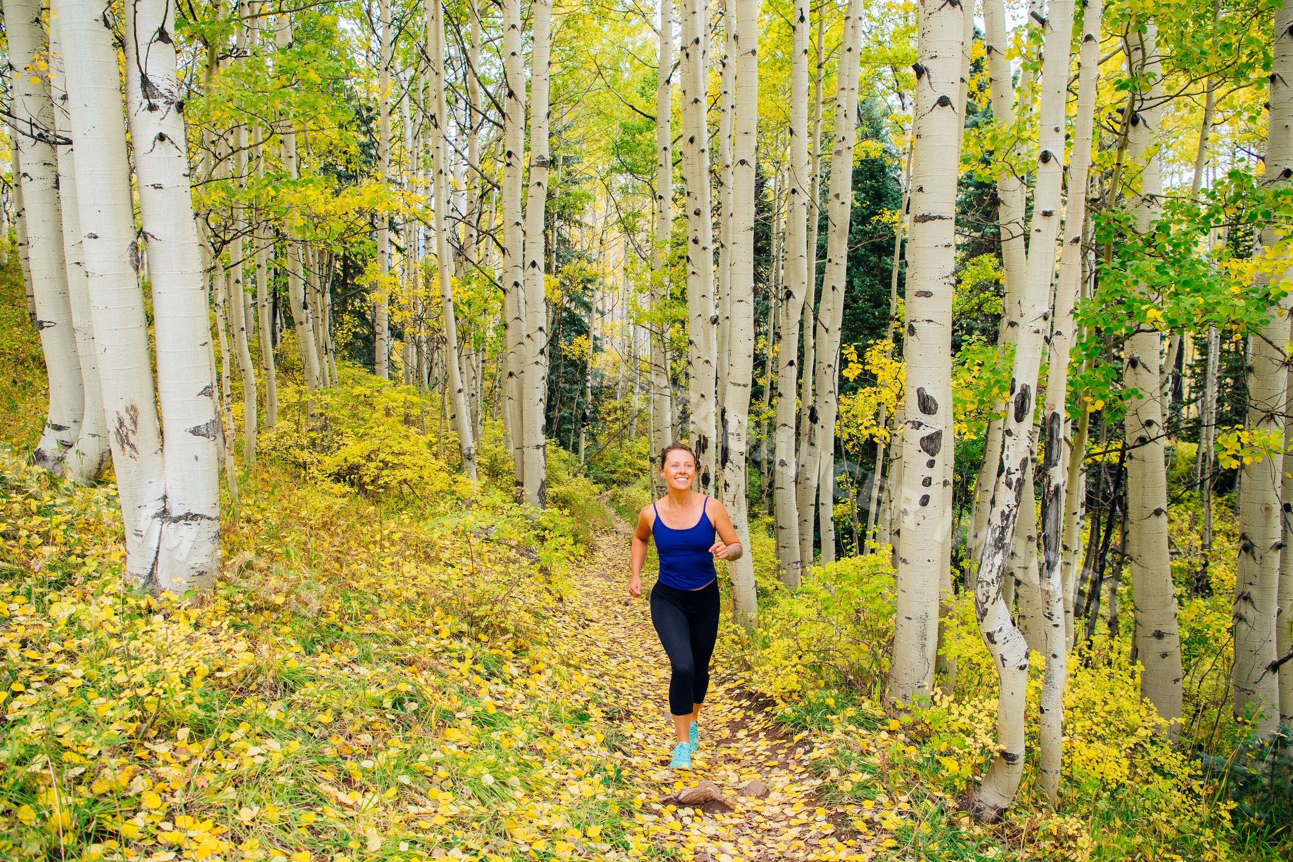 White woman running on fall trail through aspen forest