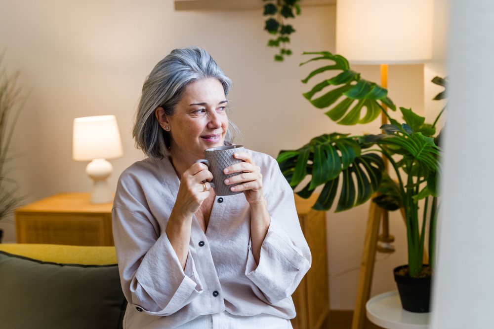 White woman holding mug and smiling in cozy indoor setting
