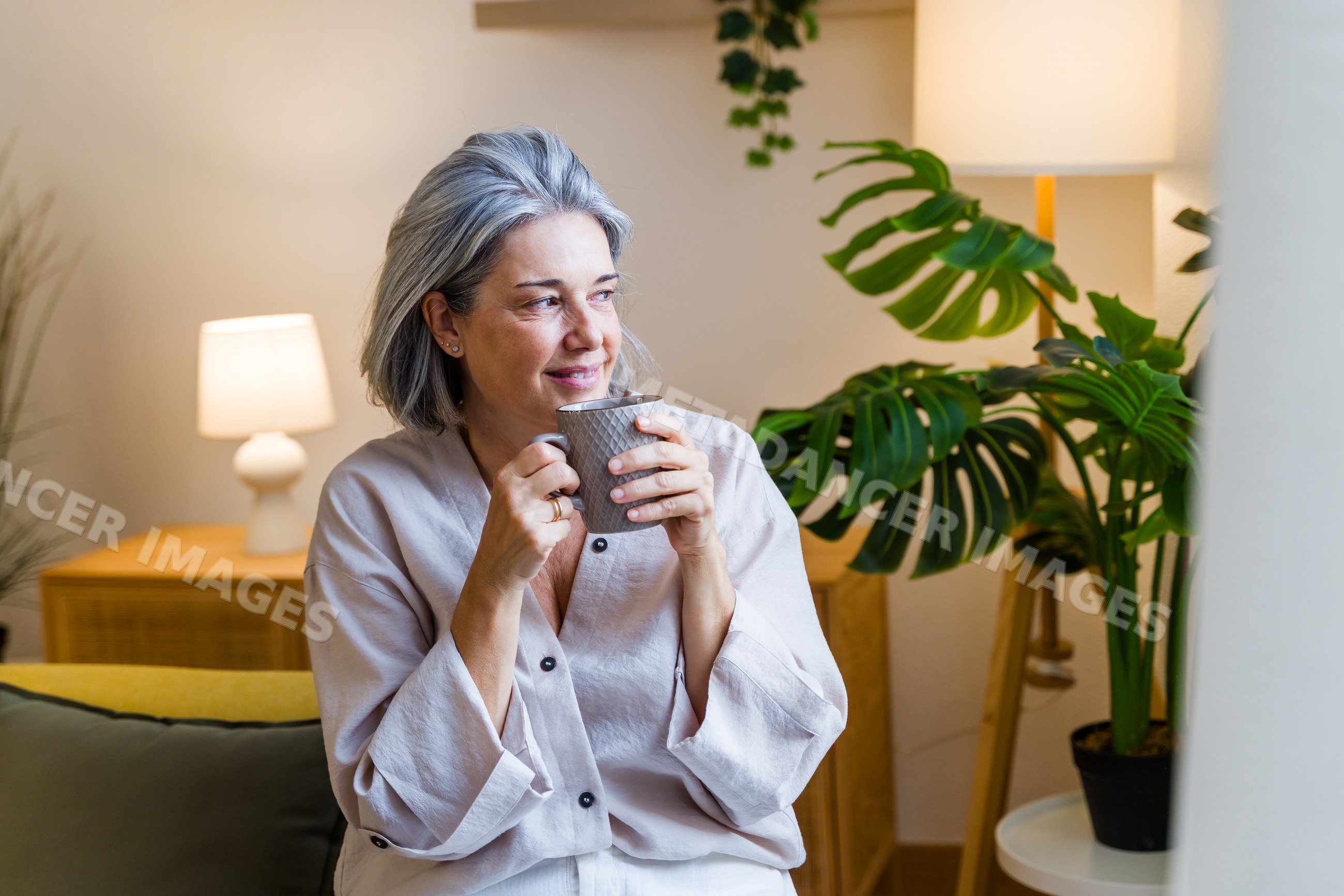 White woman holding mug and smiling in cozy indoor setting