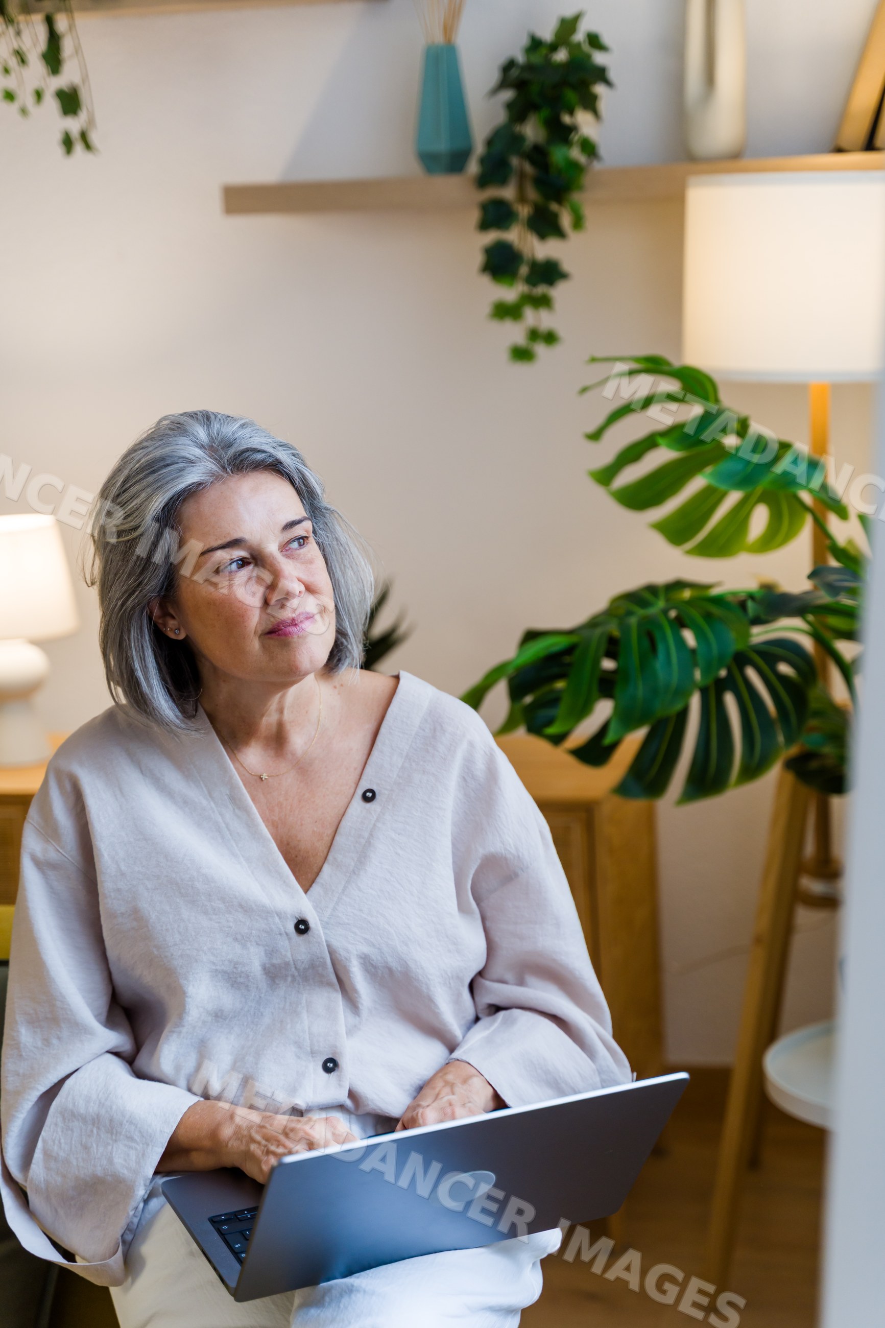 White woman using laptop sitting indoors in a modern room with plants