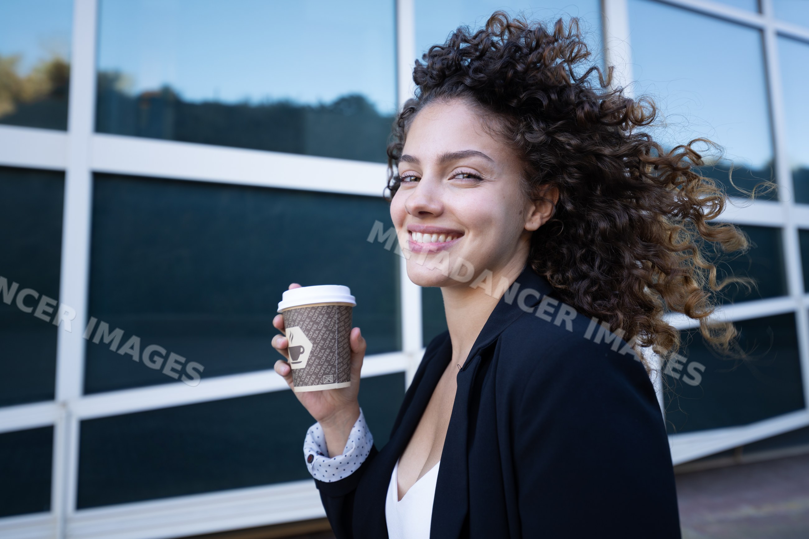 White woman with curly hair holding coffee cup outdoors