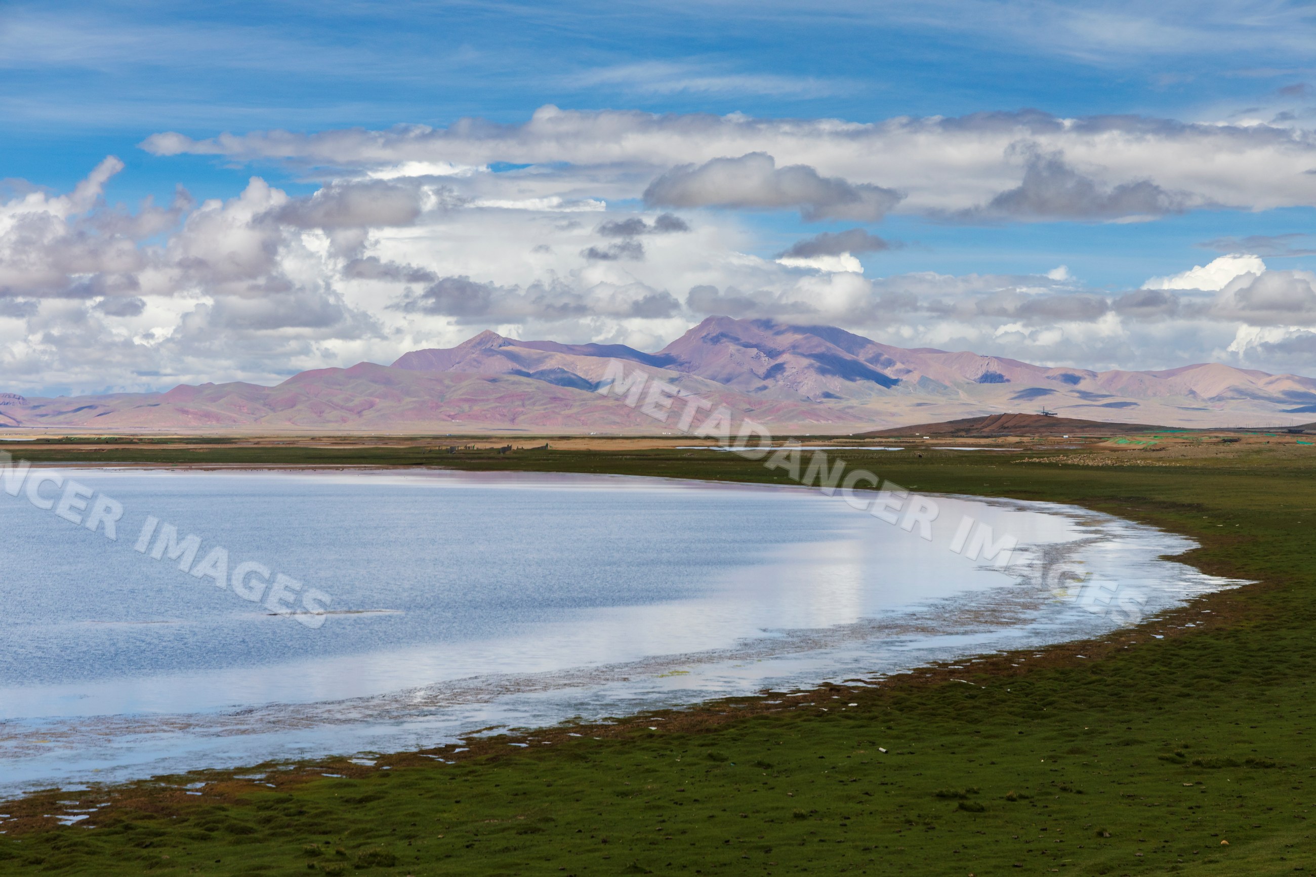 Lake with grassy shore and mountains in Kham Tibet landscape