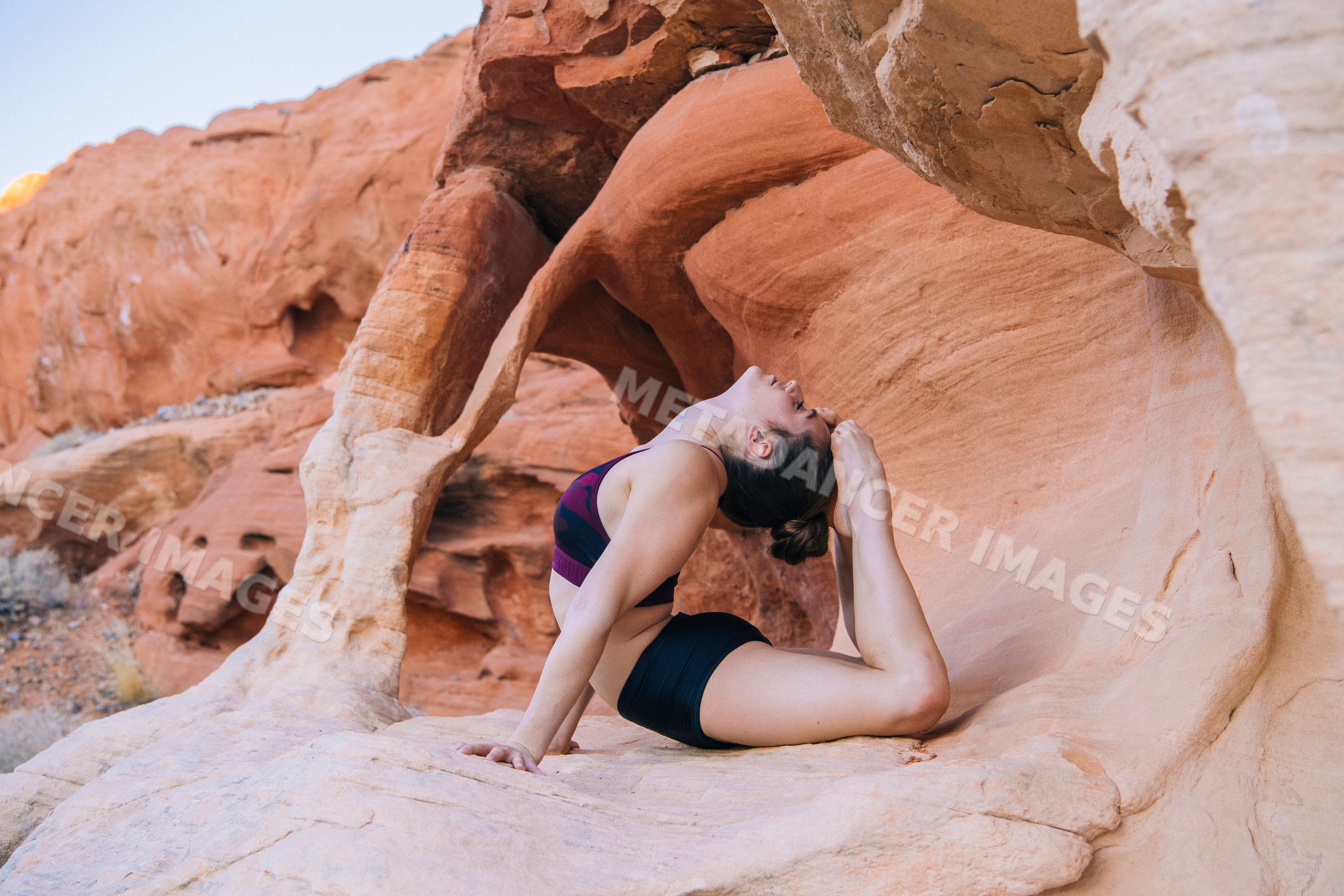 White woman practicing yoga acrobatics on rock formation