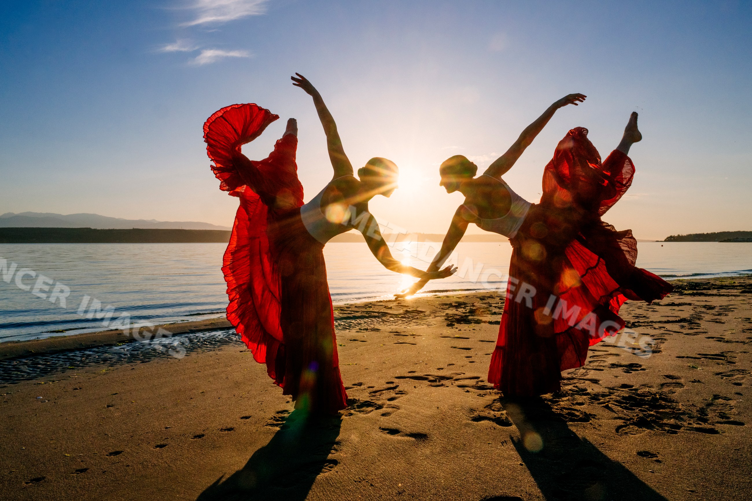 Two white women doing partner acrobatics yoga on a beach at sunset