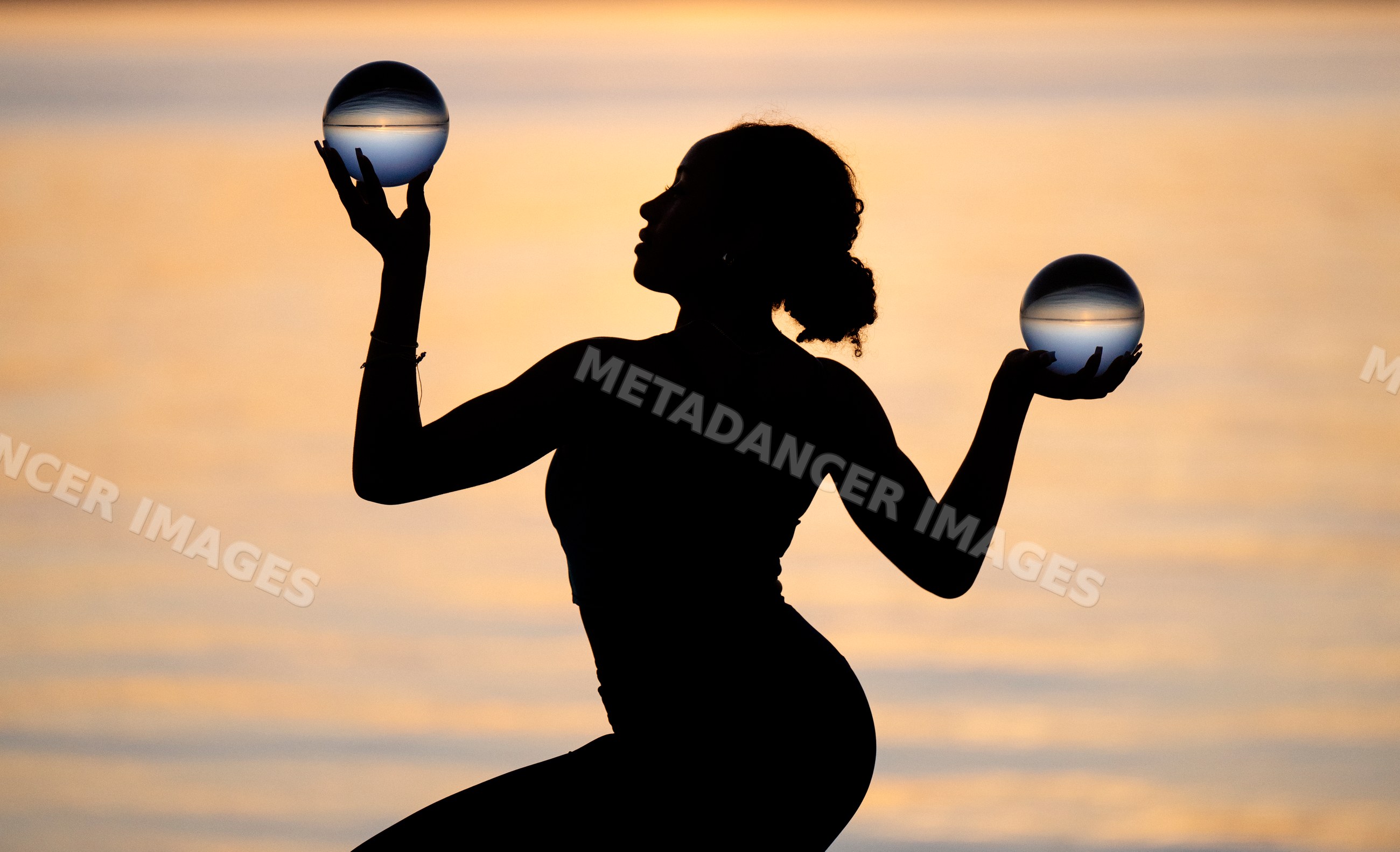 Hispanic woman practicing yoga holding glass balls at sunset by water