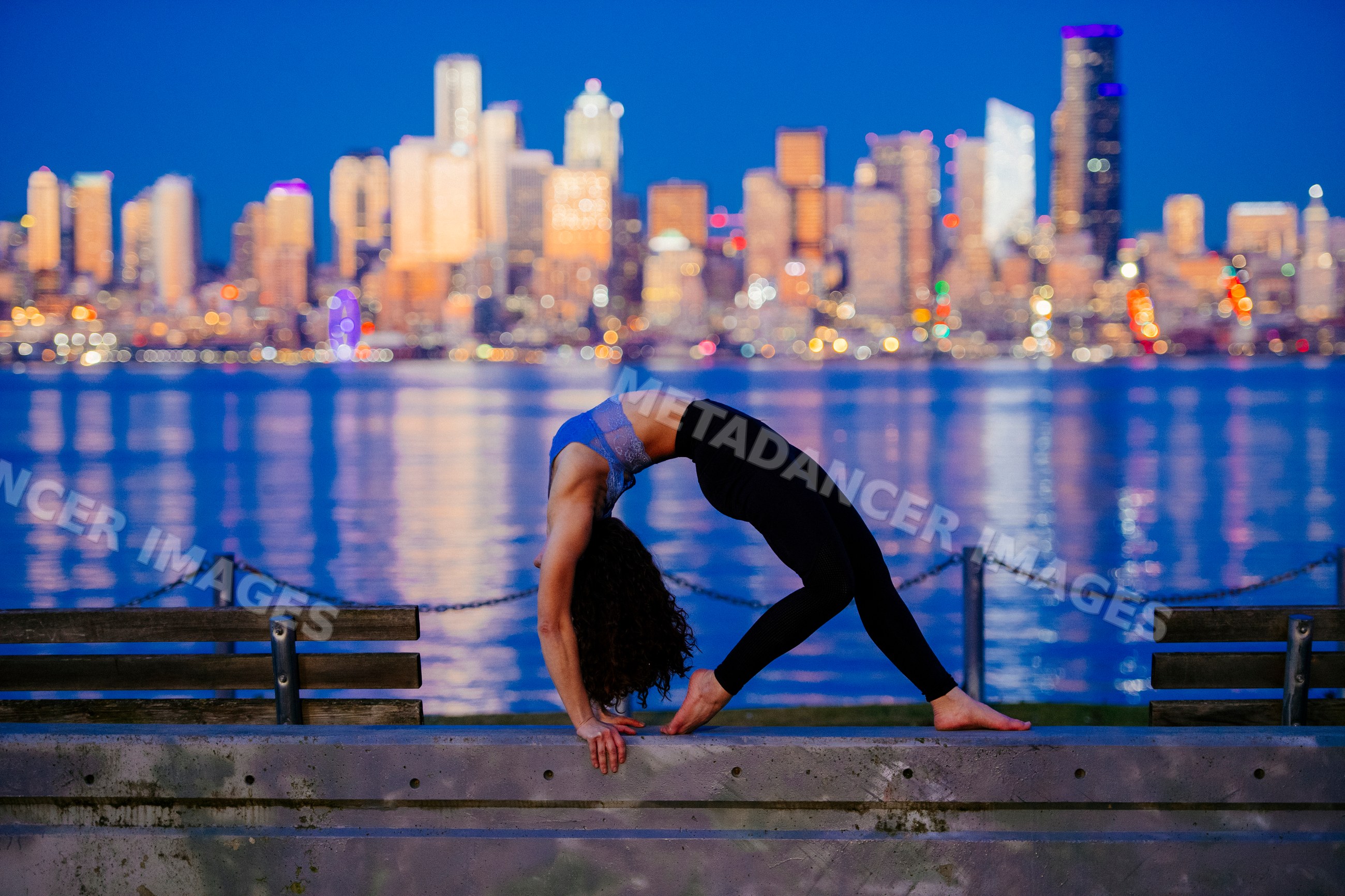 White woman doing yoga backbend by Seattle waterfront at evening