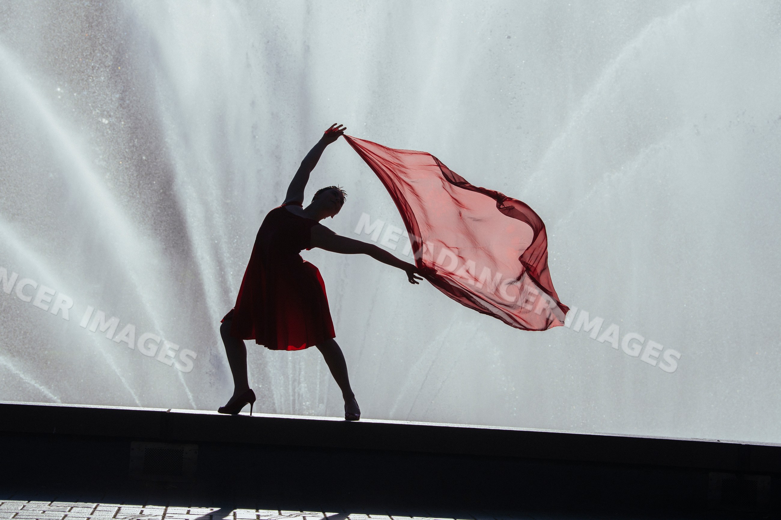 Silhouette of white dancer with red scarf by water fountain outdoors