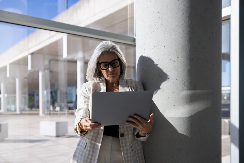 Businesswoman reading laptop by concrete column in modern outdoor
