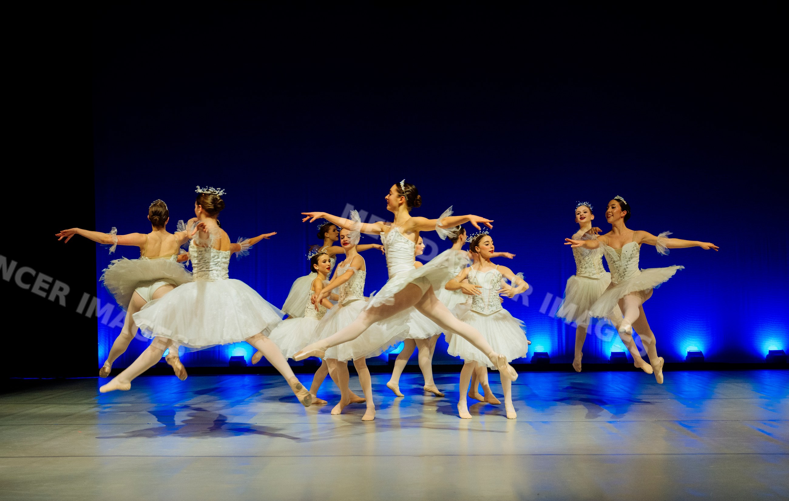 Ballet dancers perform a group routine in white tutus on stage