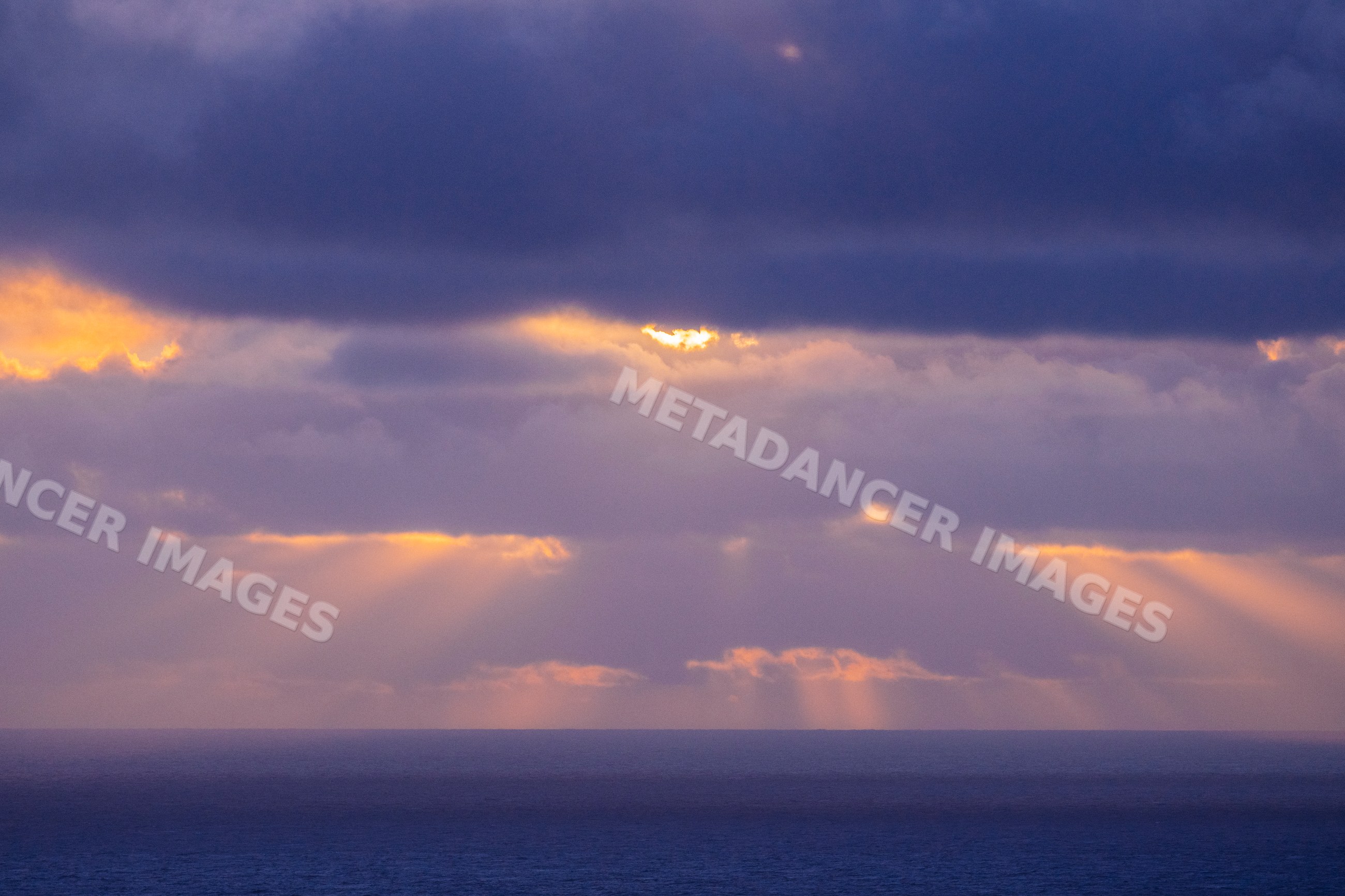 Sunlight piercing clouds over ocean horizon at sunrise in California