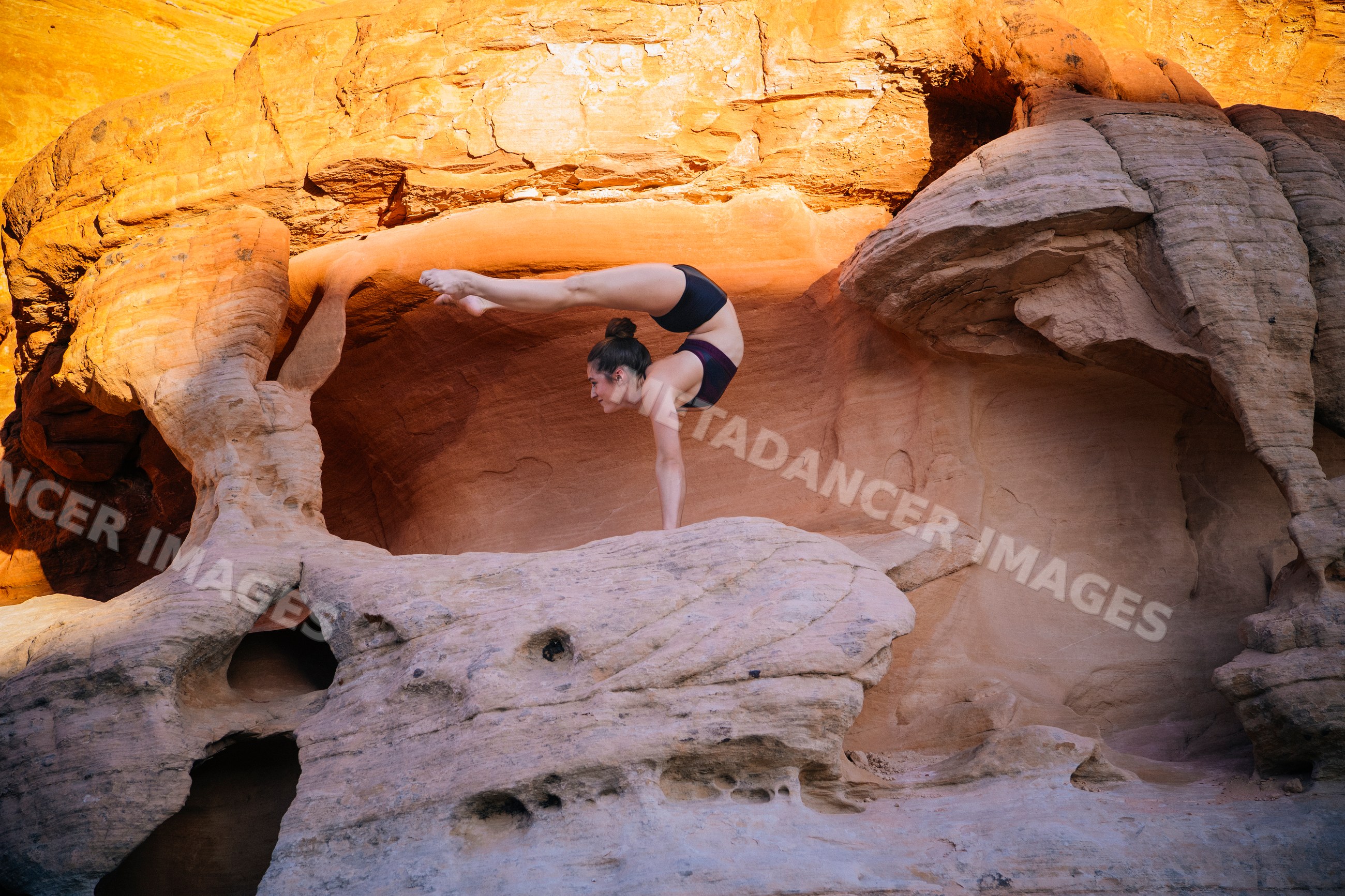 White woman performing handstand yoga pose on rock formation outdoors