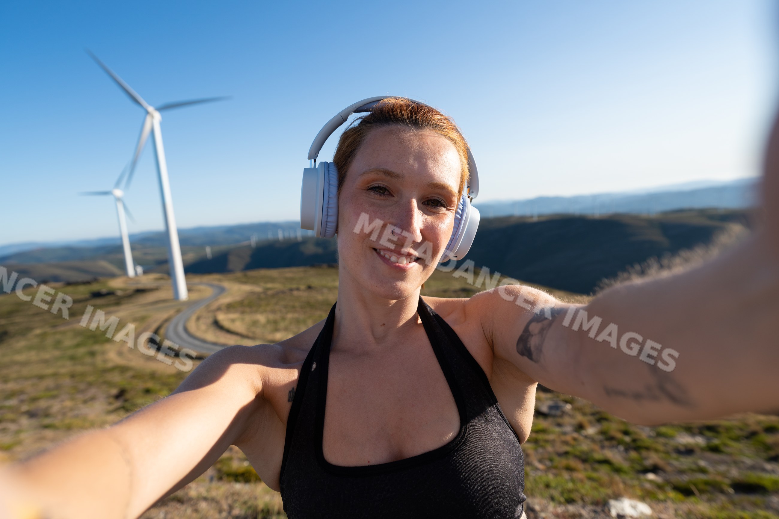 A white woman wearing headphones taking a selfie outdoors