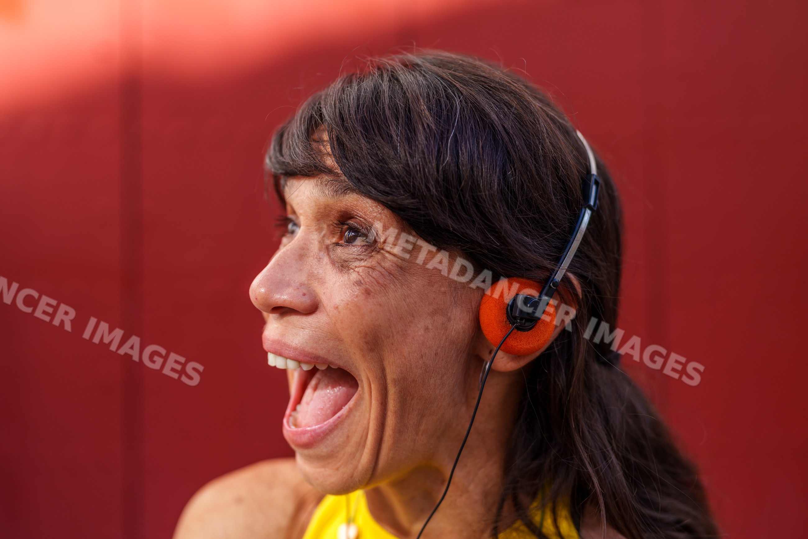 Hispanic woman talking with orange headphones against red background