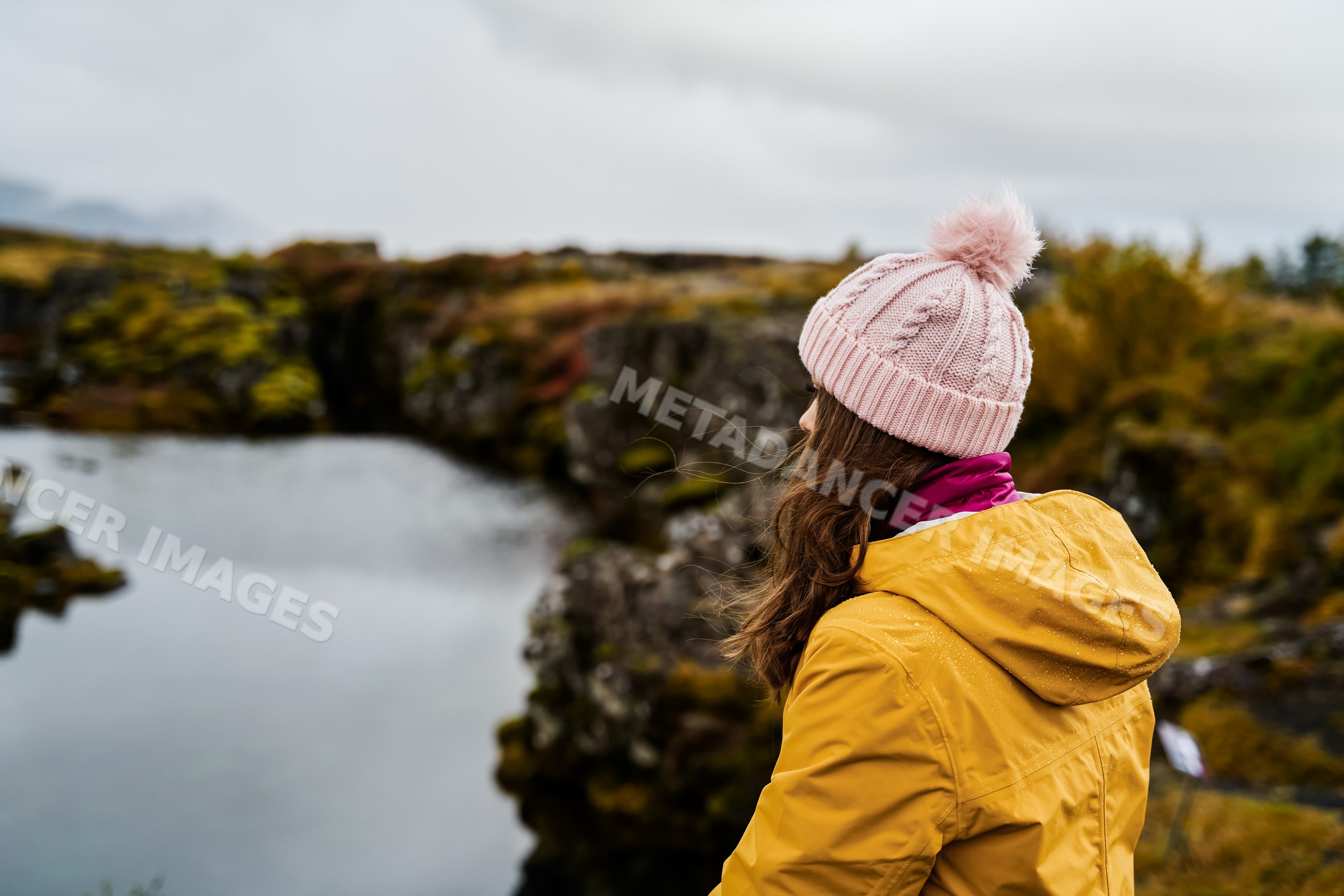 White Woman wearing a yellow jacket looks over a lake