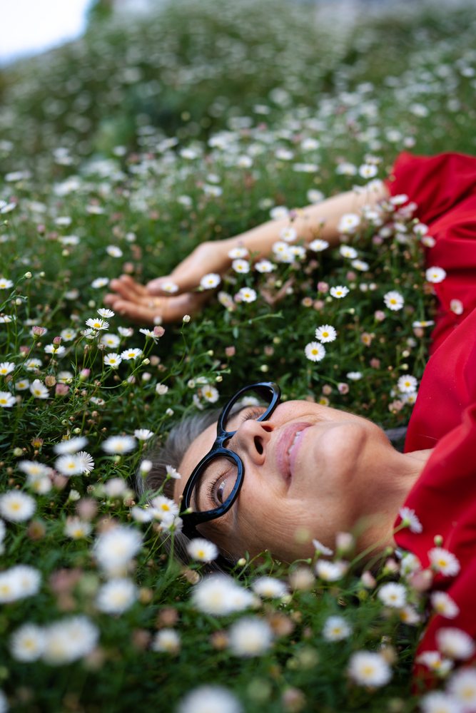 White woman lying in field of daisies wearing glasses