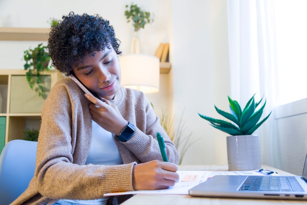 African American woman multitasks on phone call and note taking