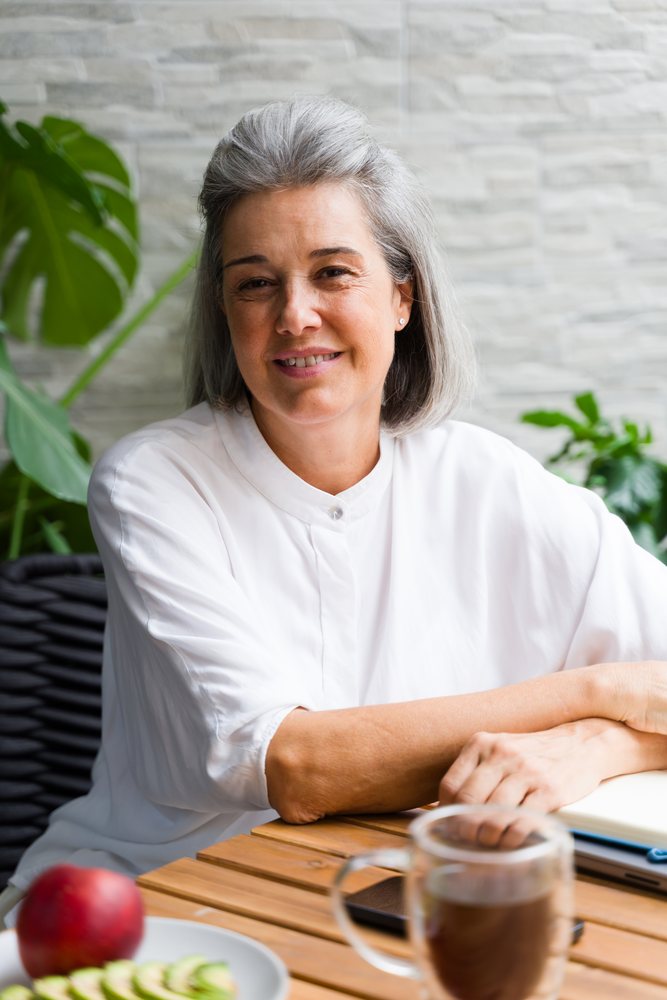 Middle-aged white woman sitting at a table with coffee and fruit