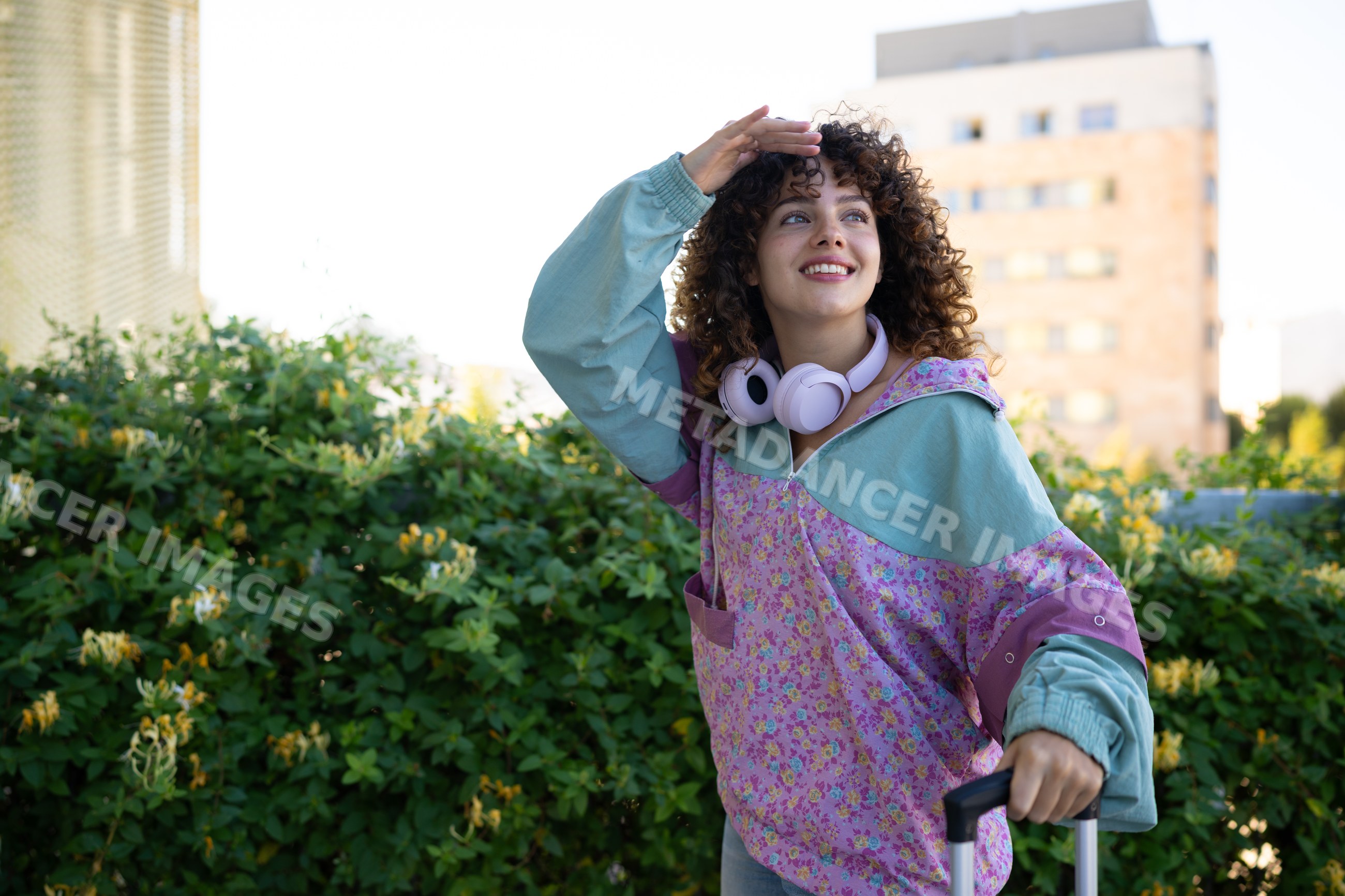 White woman smiling outdoors with suitcase and headphones in city