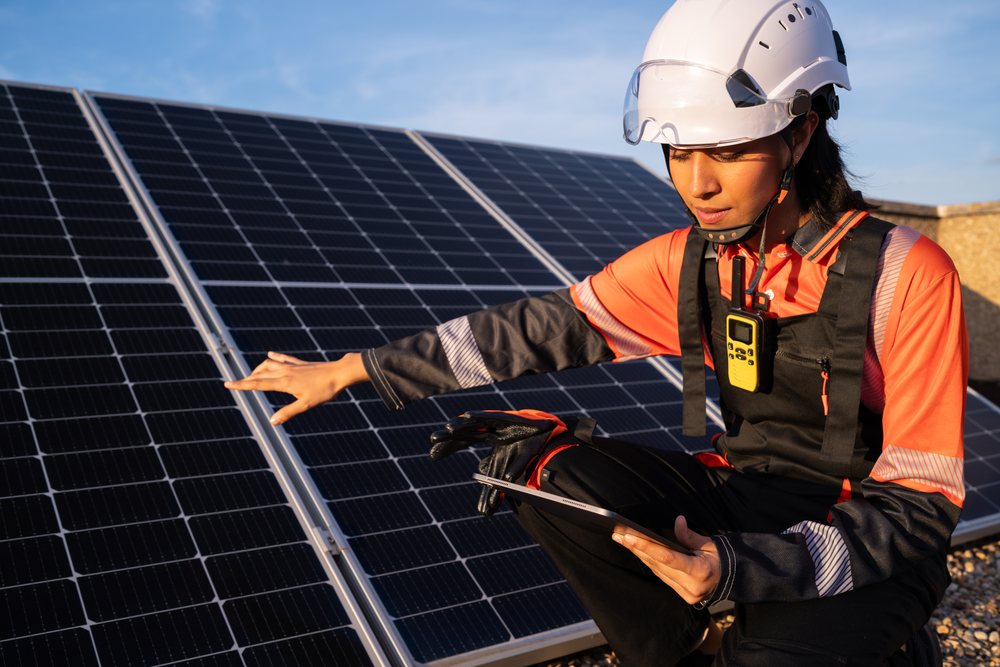 Hispanic woman technician inspecting solar panels with tablet