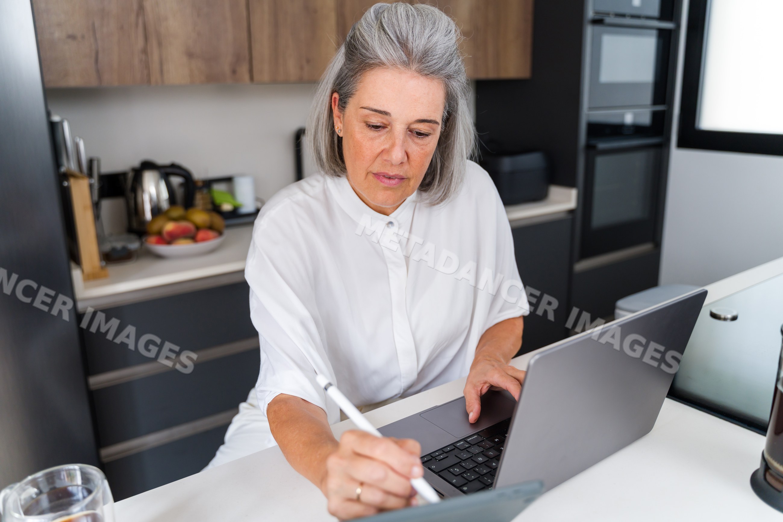 White Woman working with laptop and tablet in modern kitchen in Spain