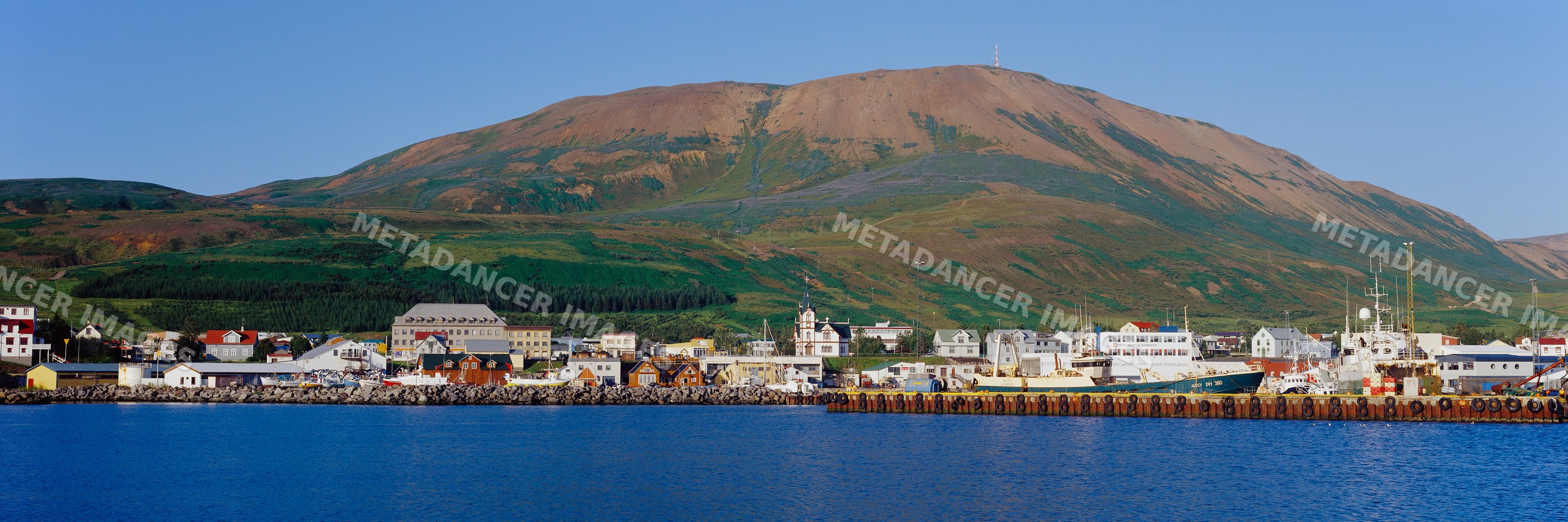 Fishing boats docked in small harbor by mountainous coastal town
