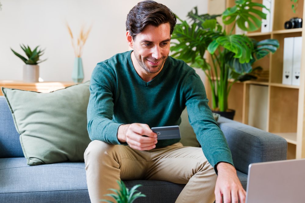White man using credit card on couch at home