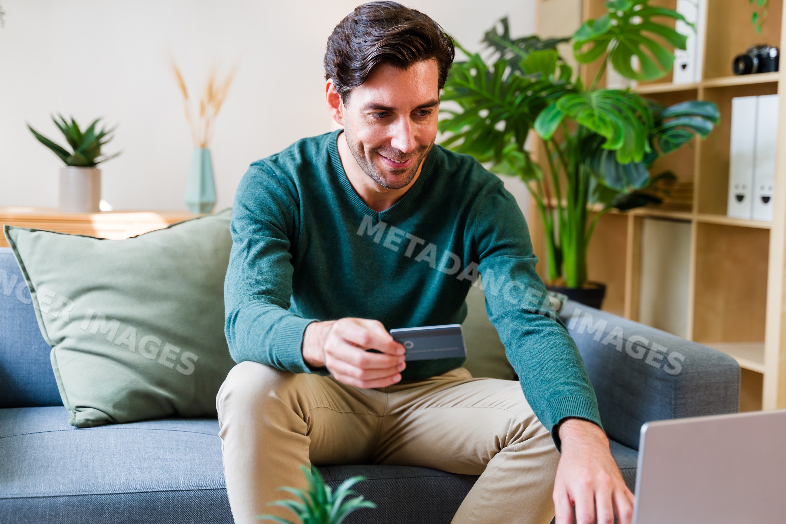 White man using credit card on couch at home