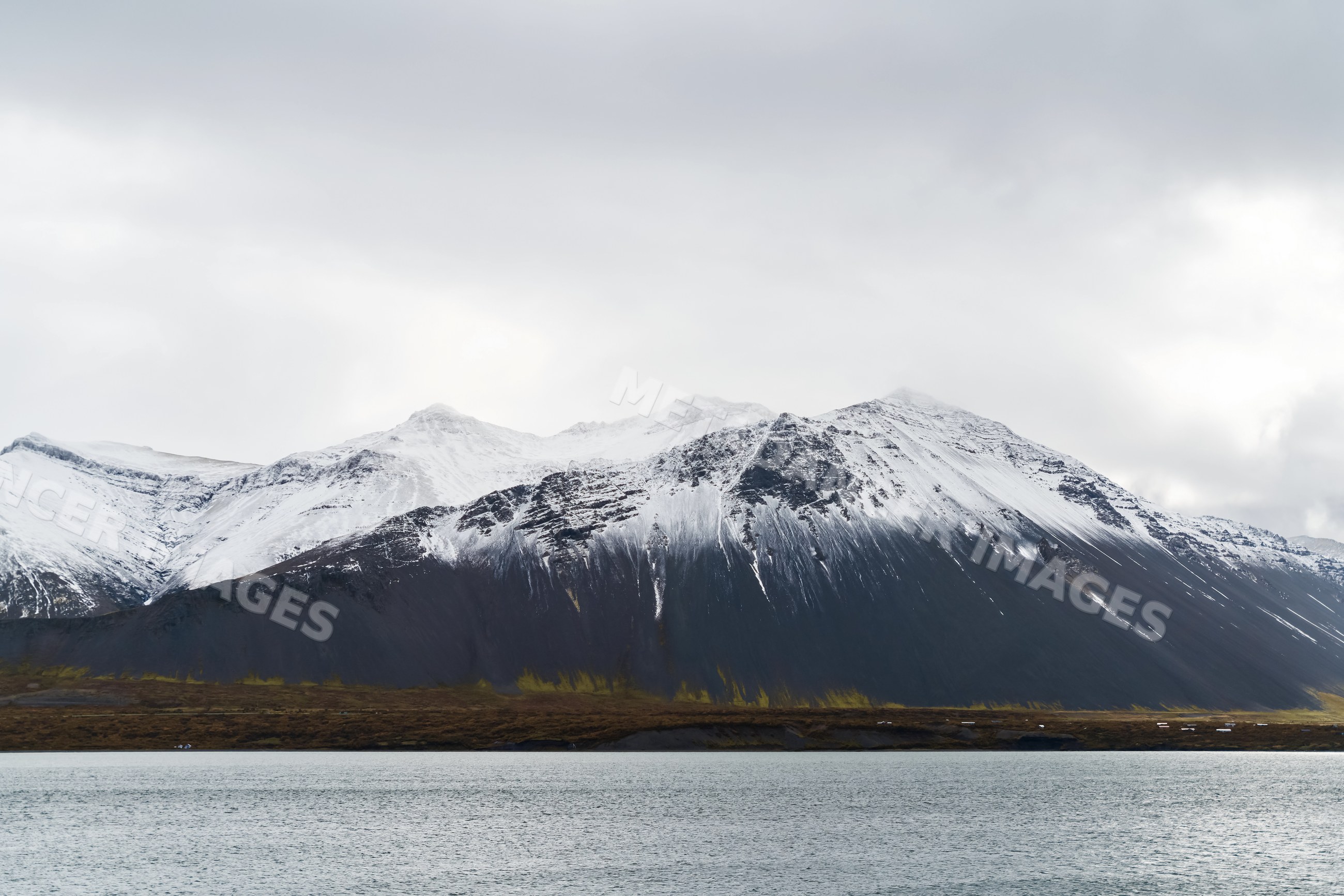 Snowy mountains beside calm water under overcast sky