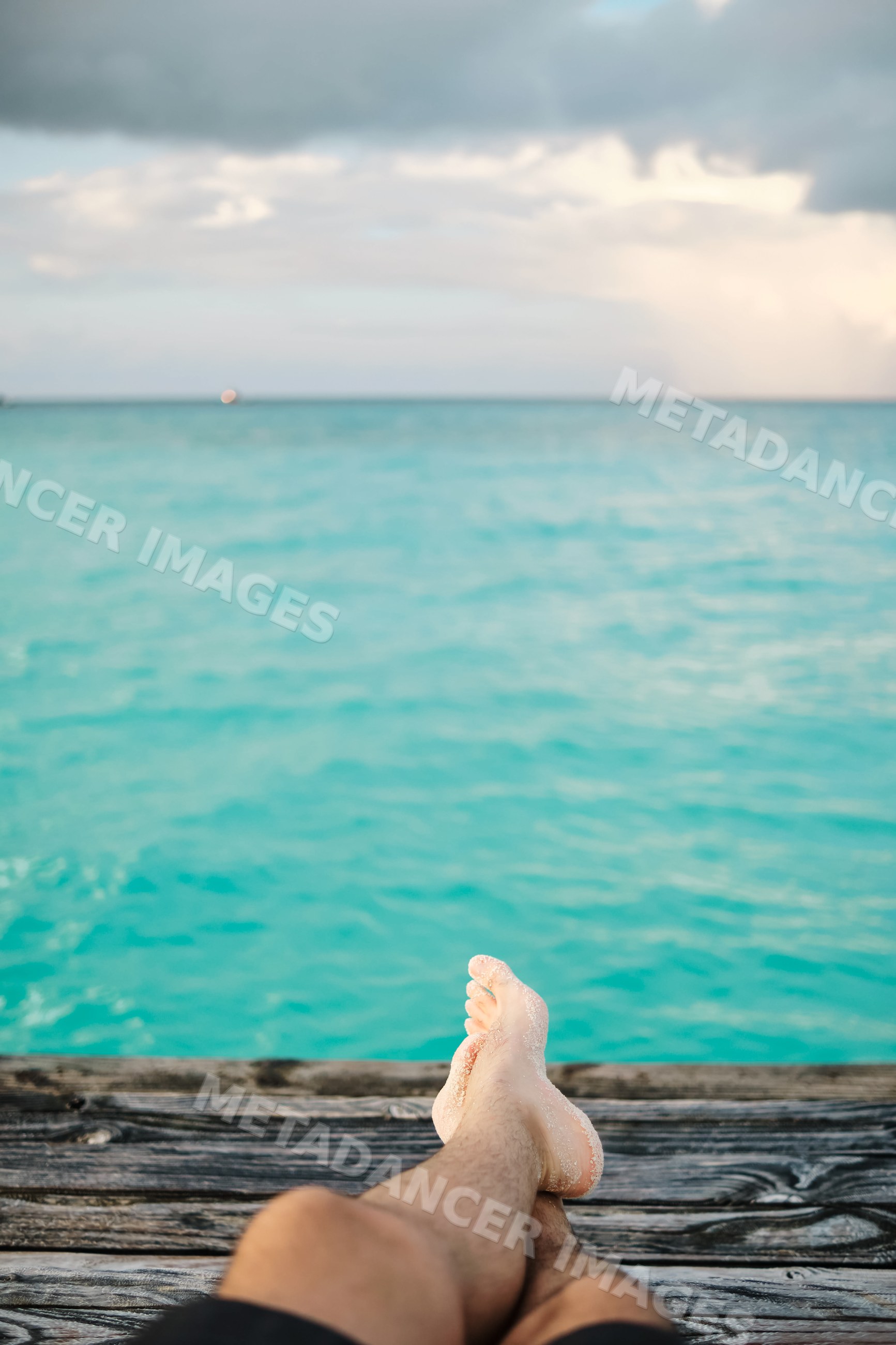 A person relaxes with sandy feet on a dock overlooking the turquoise