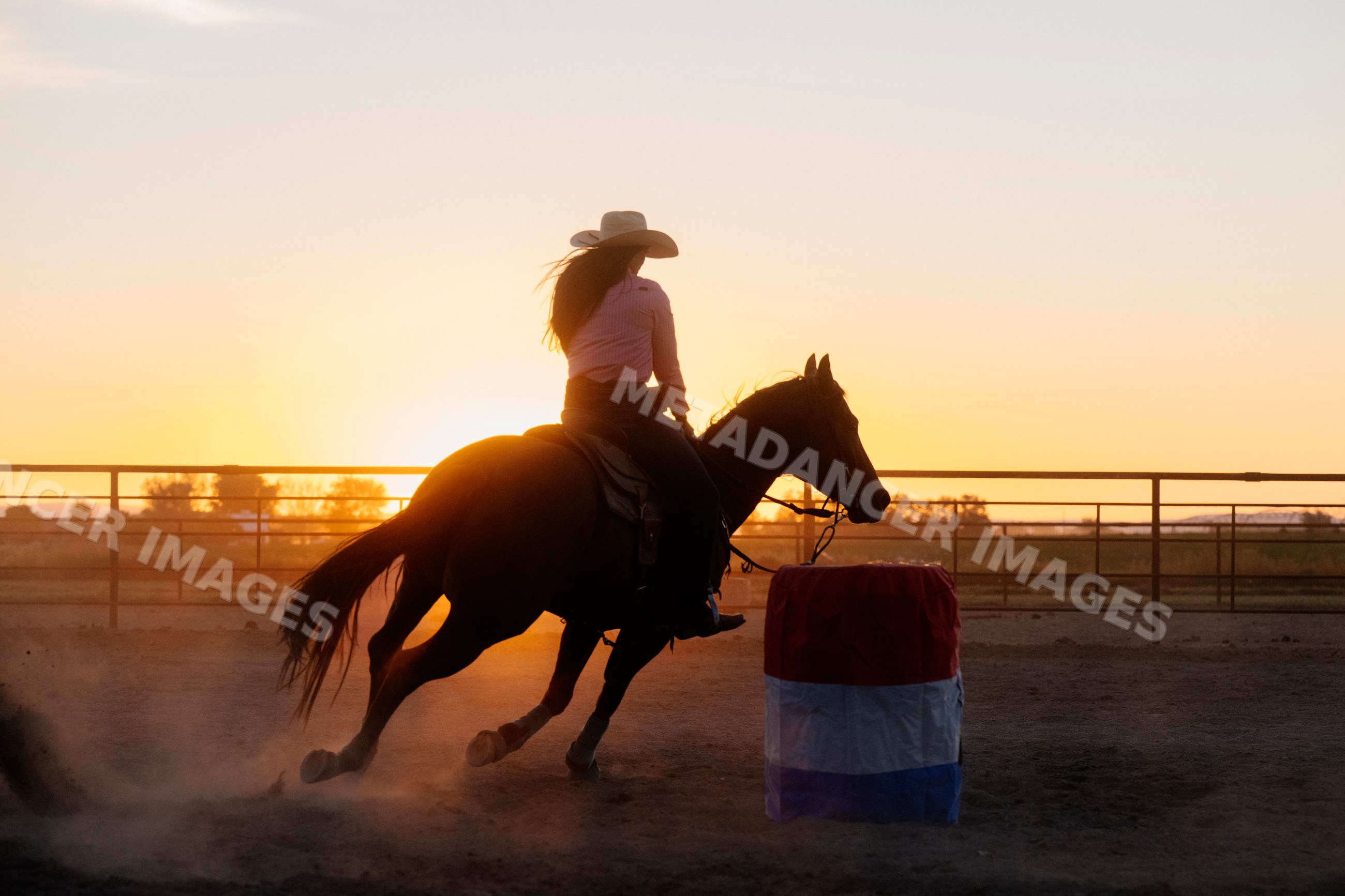 Cowgirl riding horse in barrel racing at sunset in outdoor arena