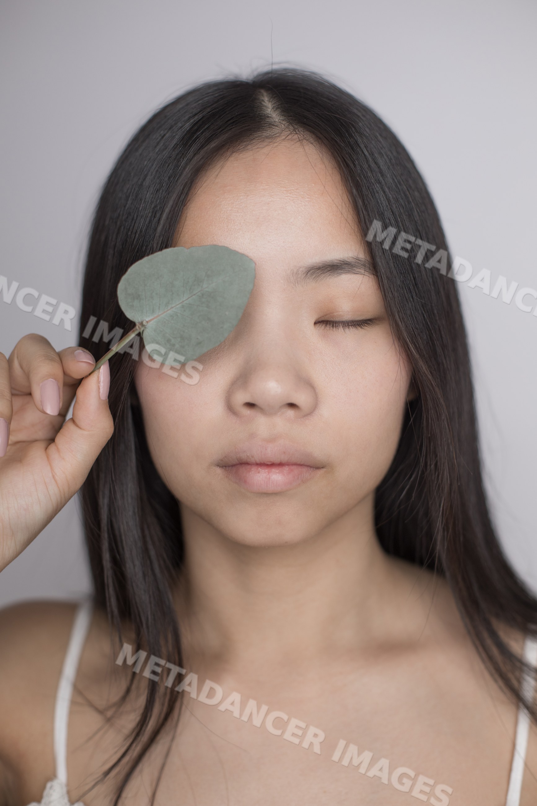 Southeast Asian woman holding a leaf over one eye