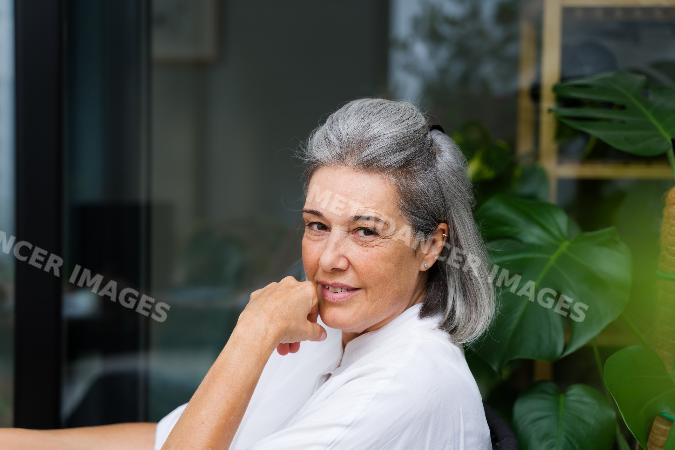 Middle-aged white woman with gray hair smiling indoors by houseplant