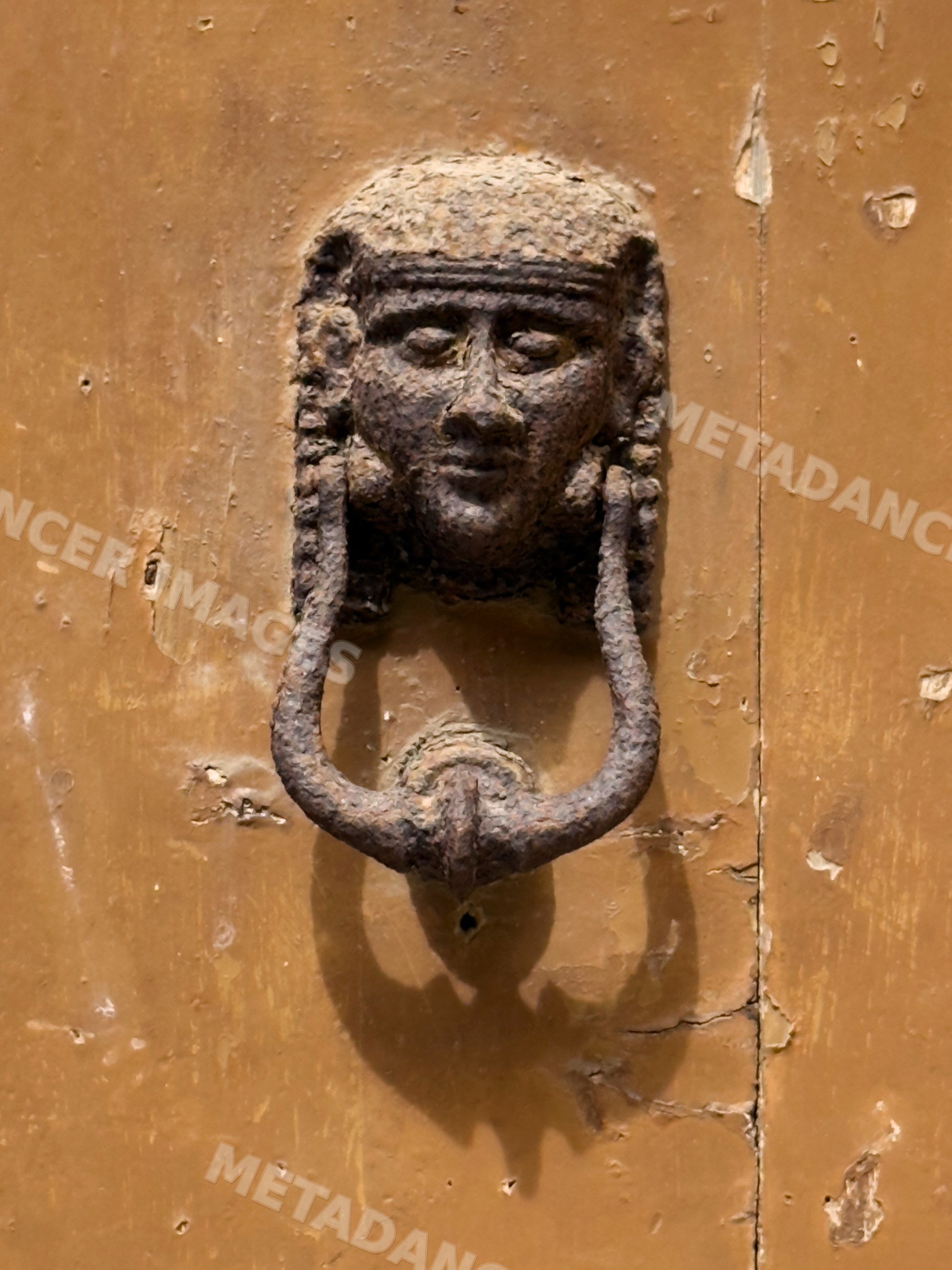 Weathered metal Door Knocker with face on old brown door