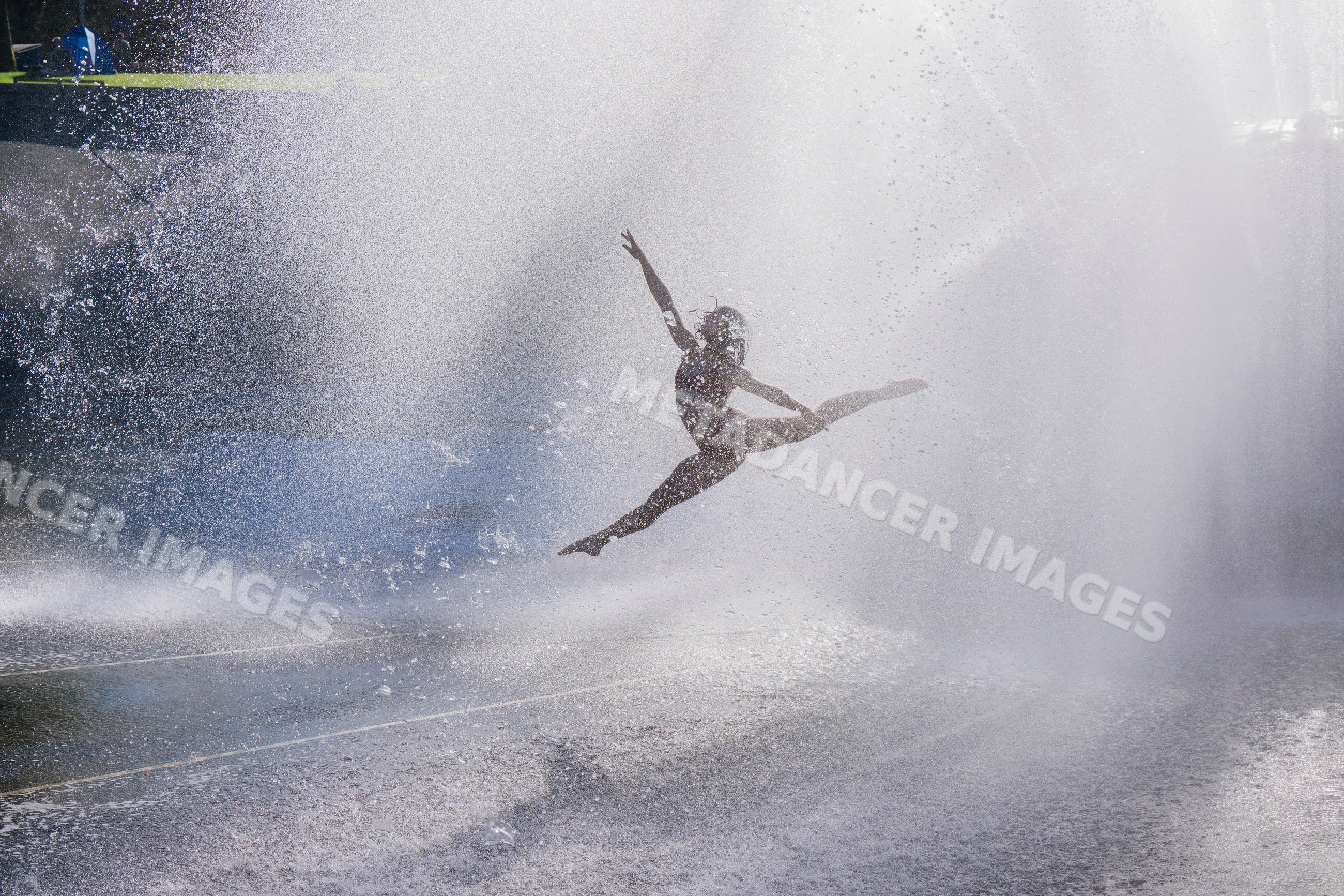 White dancer performing a high leap amid water spray outdoors