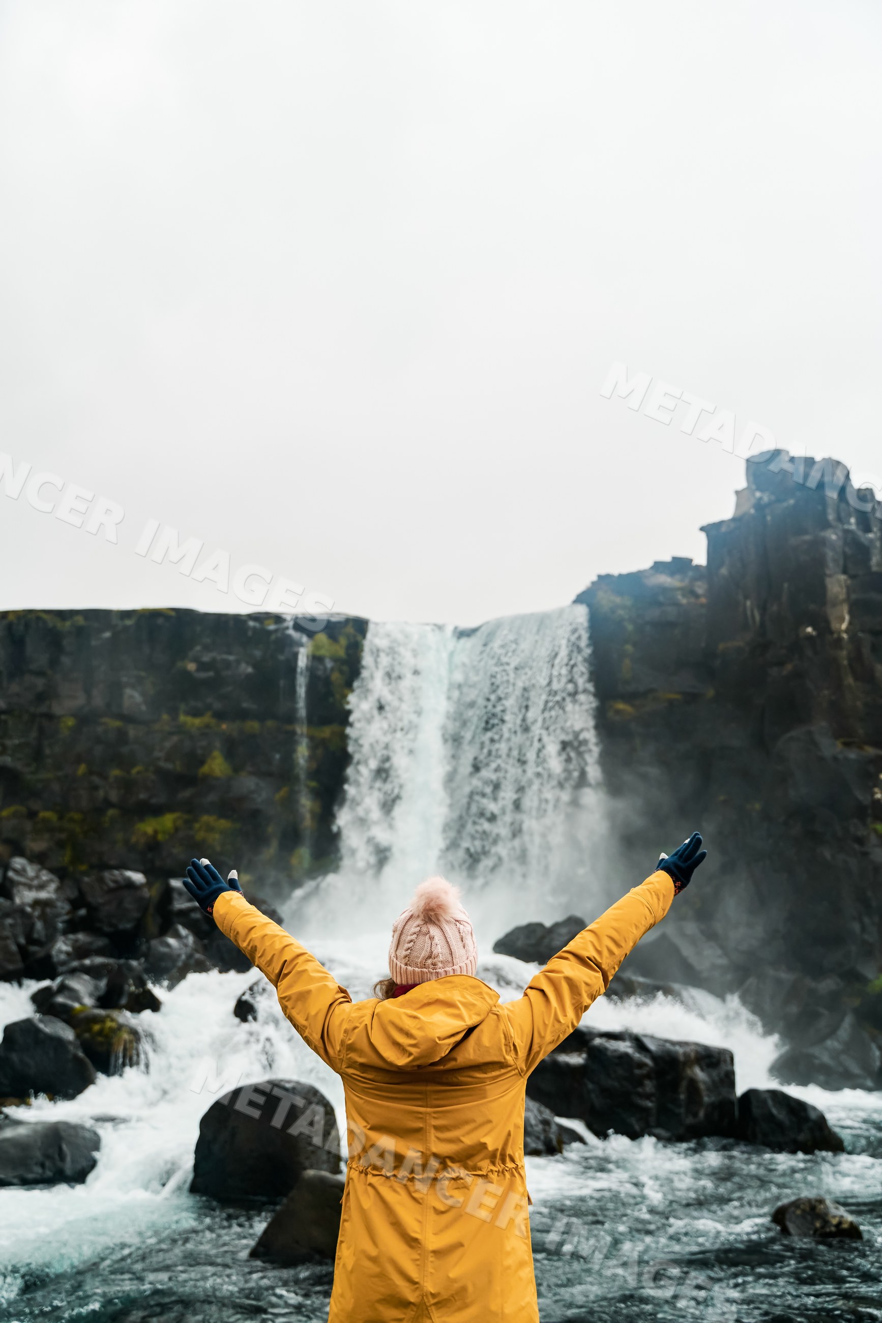 A white person with outstretched arms enjoys a waterfall