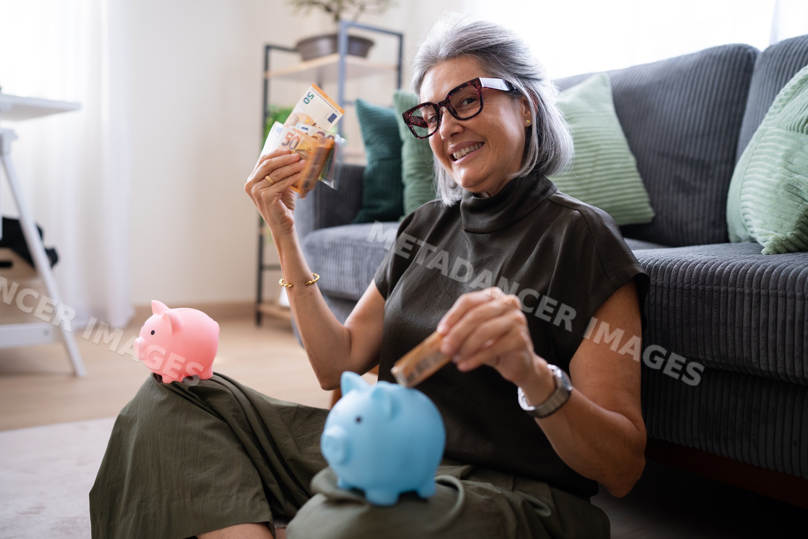 White woman saving euro banknotes in piggy banks in living room